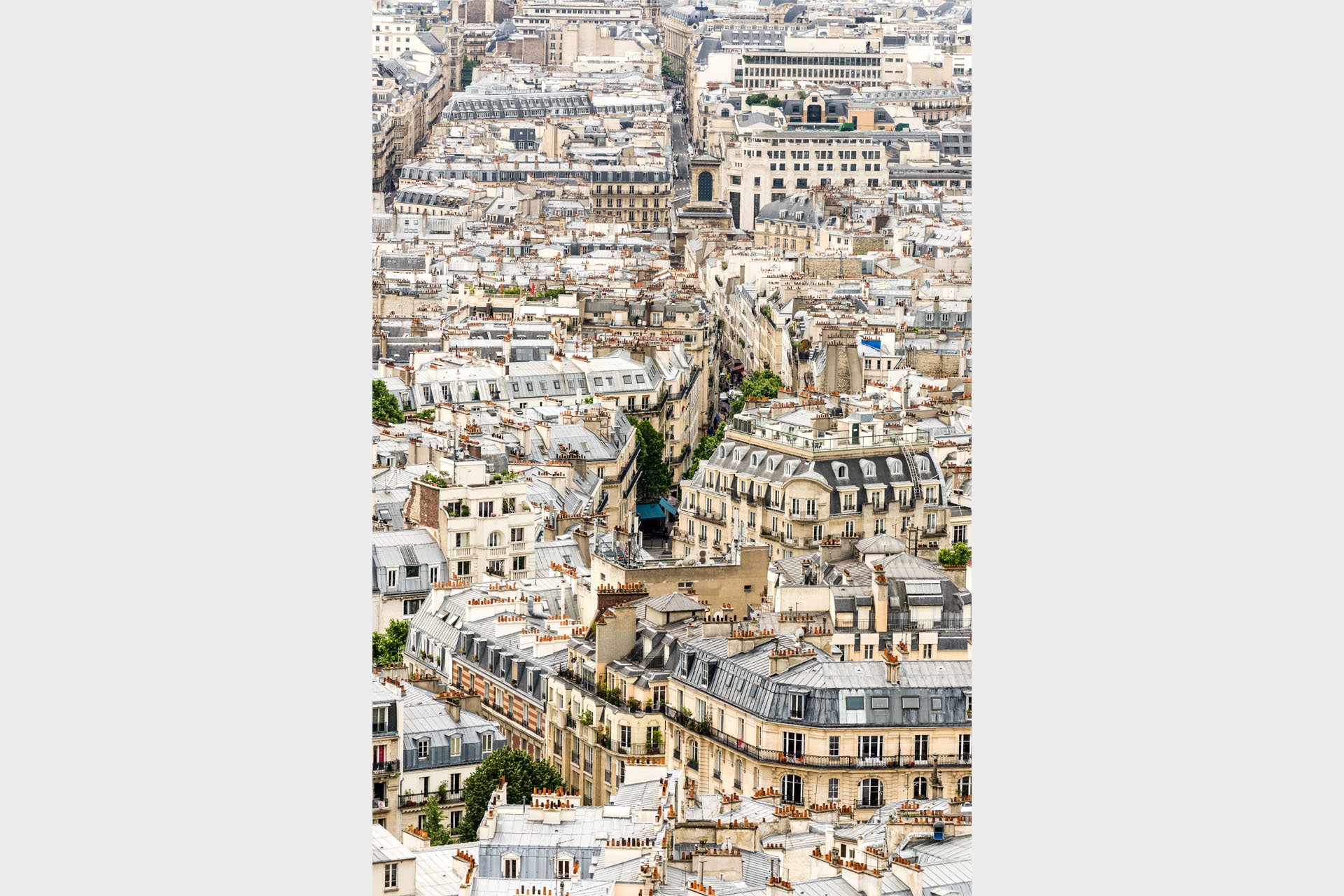 Elevated view over the rooftops of Paris, France, with cream stone apartment buildings, grey zinc roofs, terracotta chimney pots and narrow streets cutting between them.