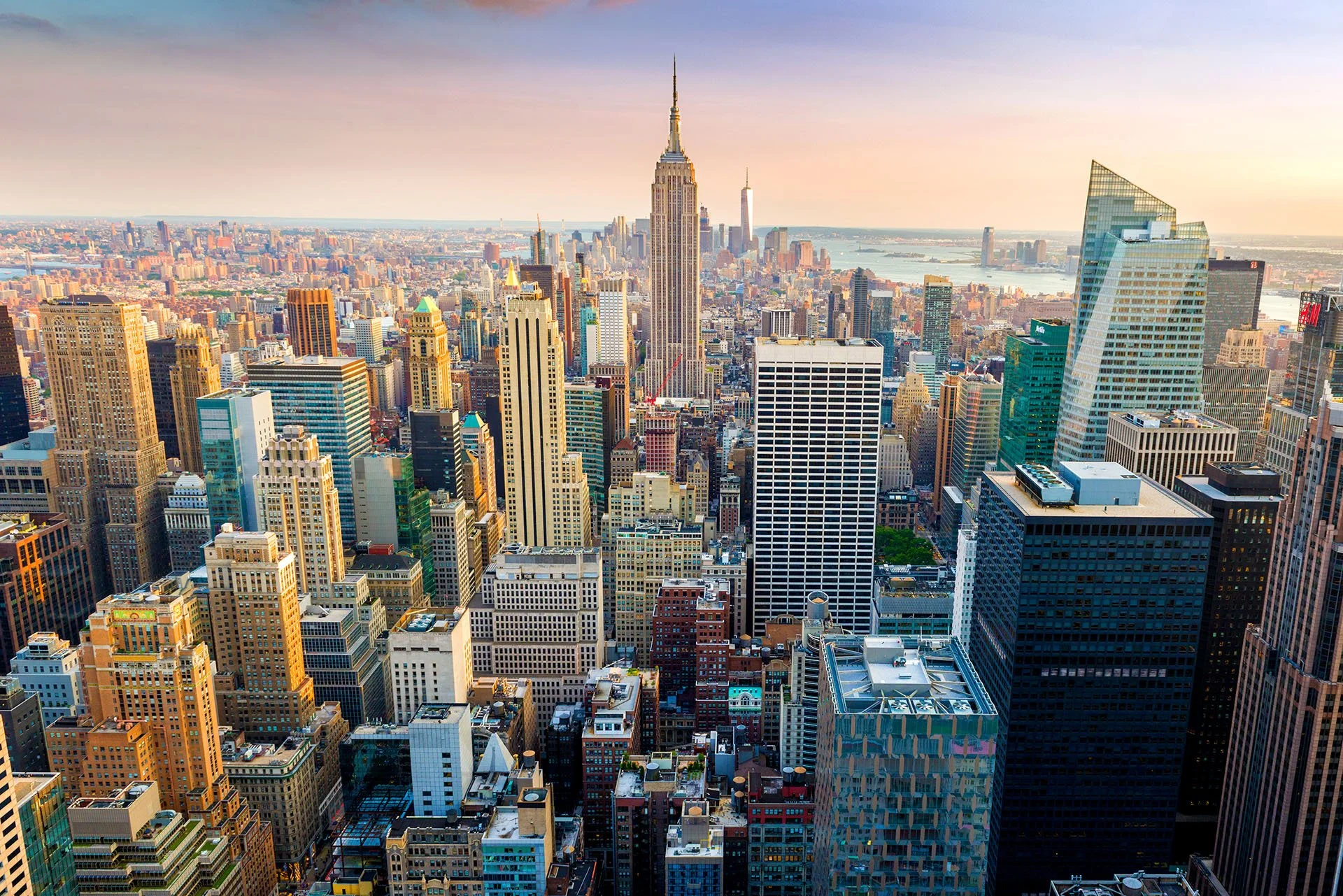 Midtown Manhattan from Top of the Rock in warm afternoon light, looking south to the Empire State Building with One World Trade Center and the Hudson River beyond, New York City.