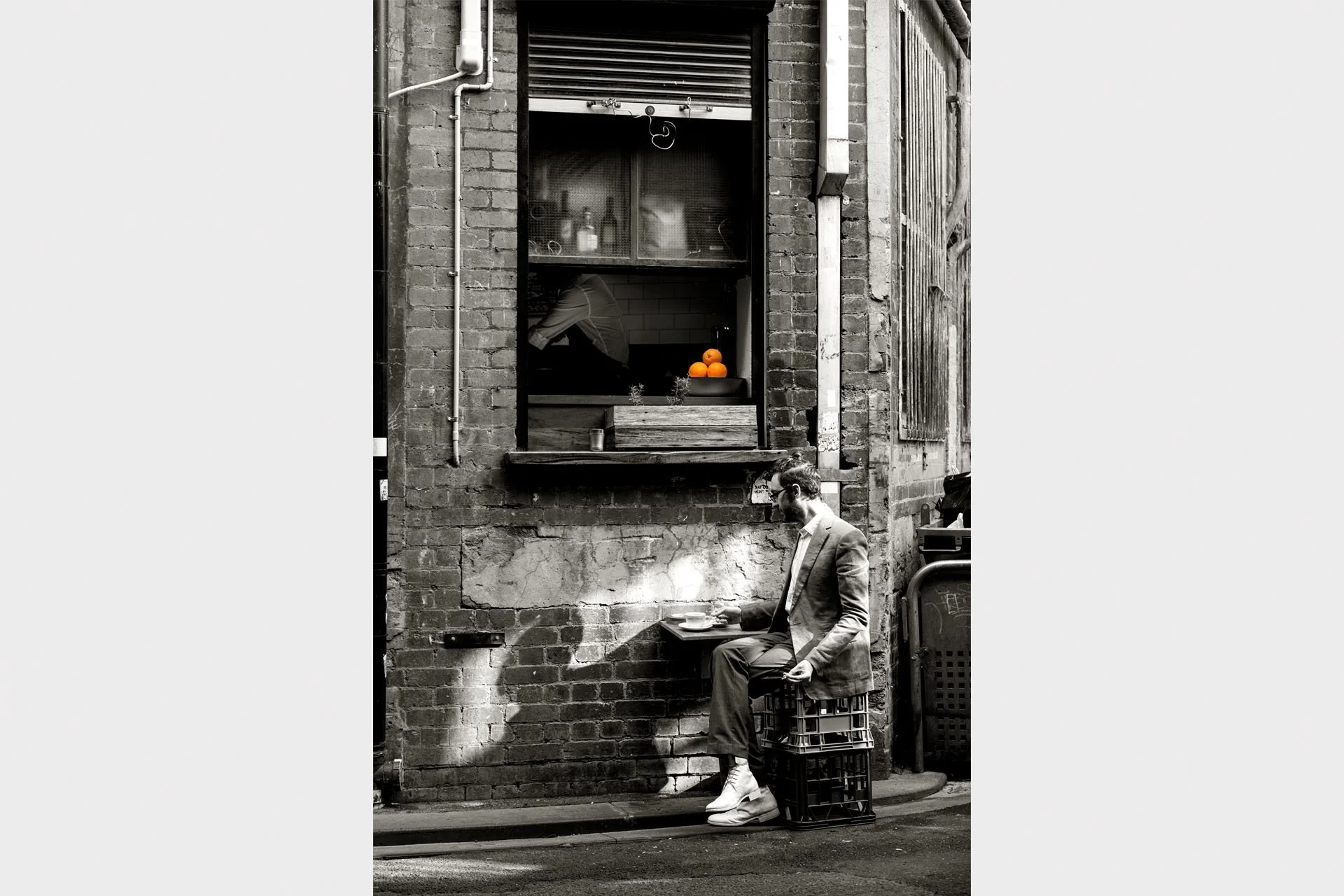 Black & white of a man drinking coffee in a laneway