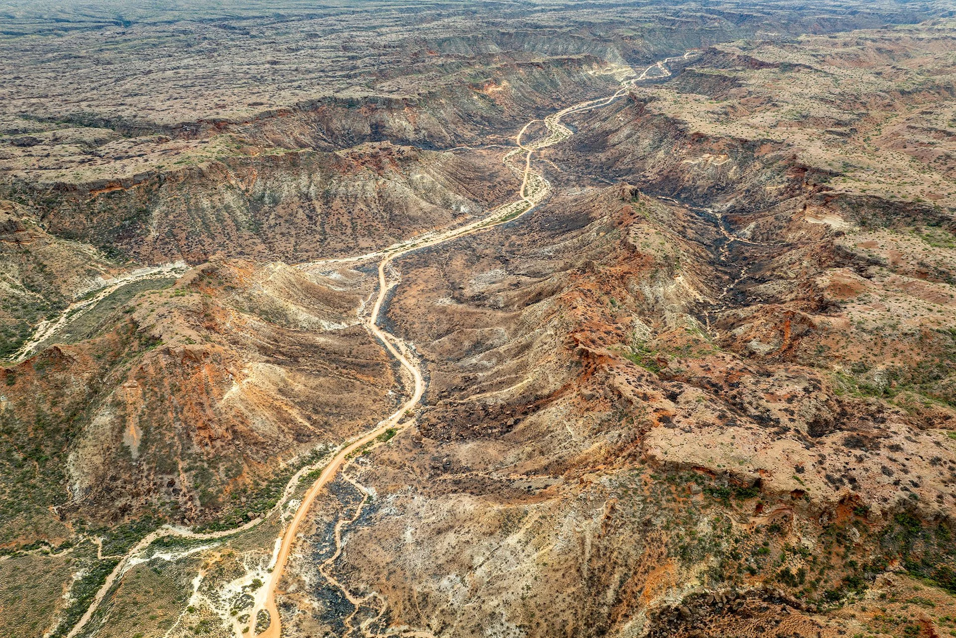 Aerial view of a dirt track winding through Shothole Canyon in Cape Range National Park near Exmouth, Western Australia, between rugged red and ochre ridges.