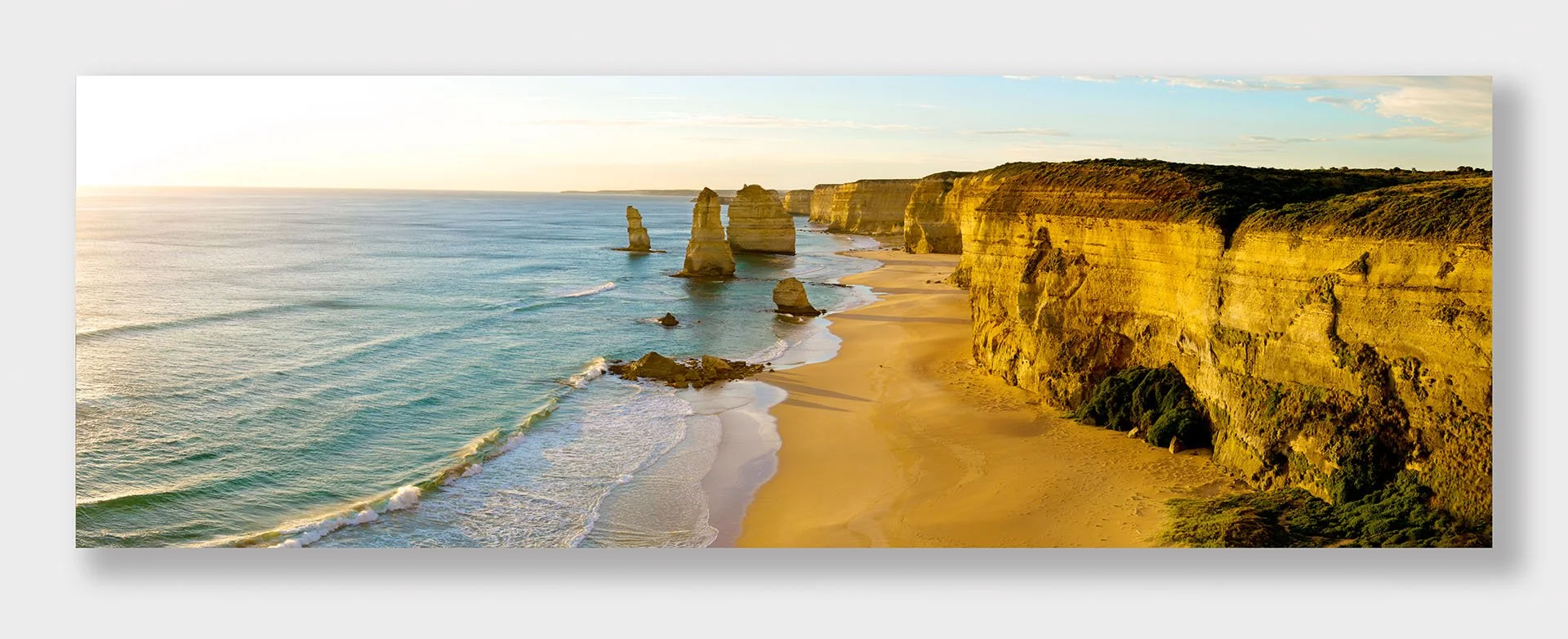 Panorama of the Twelve Apostles at sunset on the Great Ocean Road, Port Campbell National Park, Victoria, with limestone stacks and golden cliffs above a sandy beach and rolling surf.