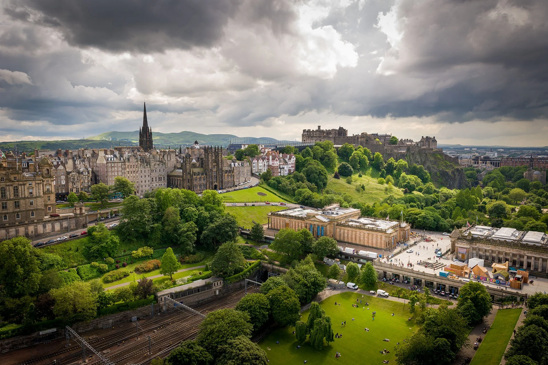 Edinburgh Castle above Princes Street Gardens and the Old Town, seen from the Scott Monument, Edinburgh, Scotland, with the National Galleries below and dark storm clouds overhead.