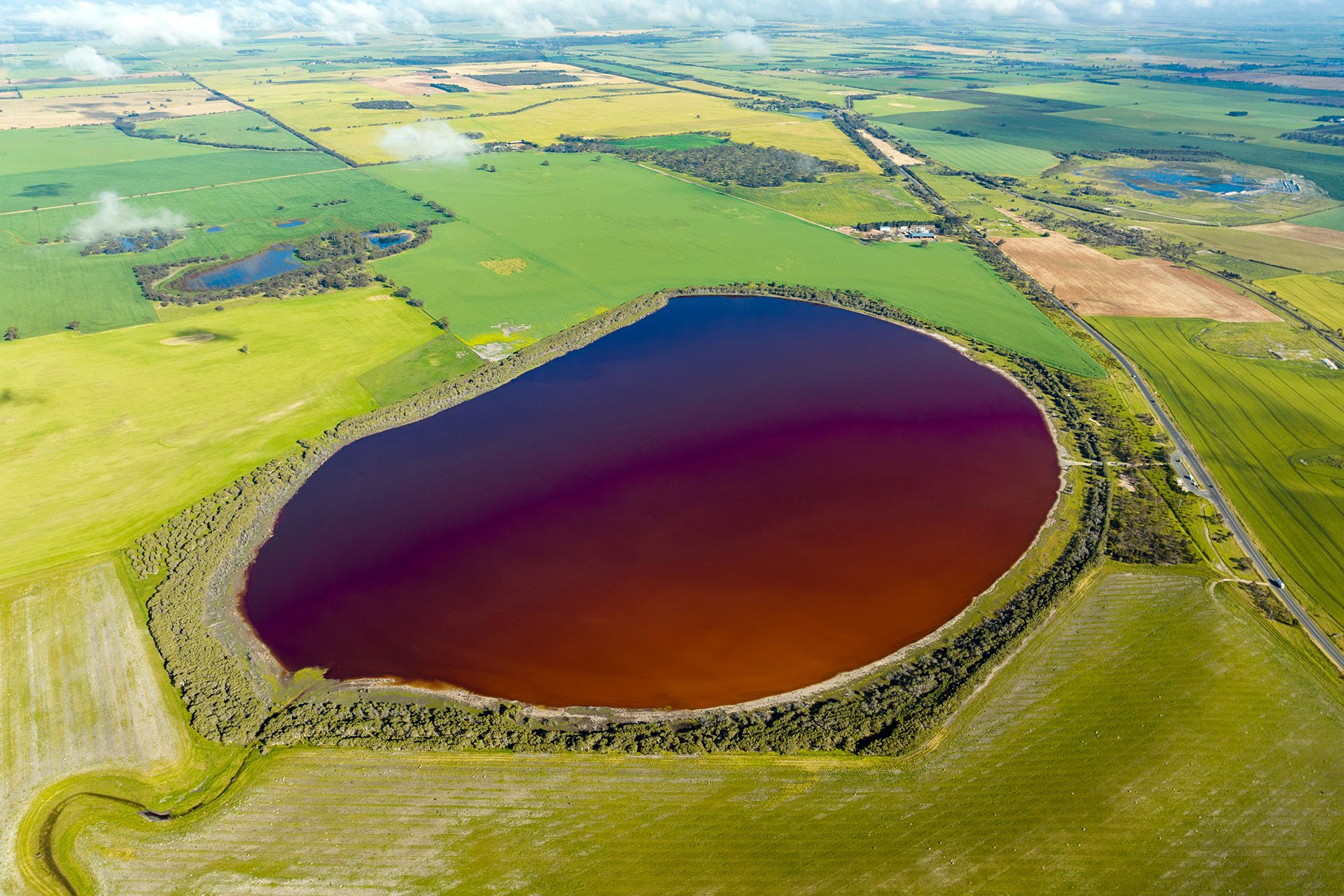 Aerial shot of a very dark Pink Lake surrounded by green fields.