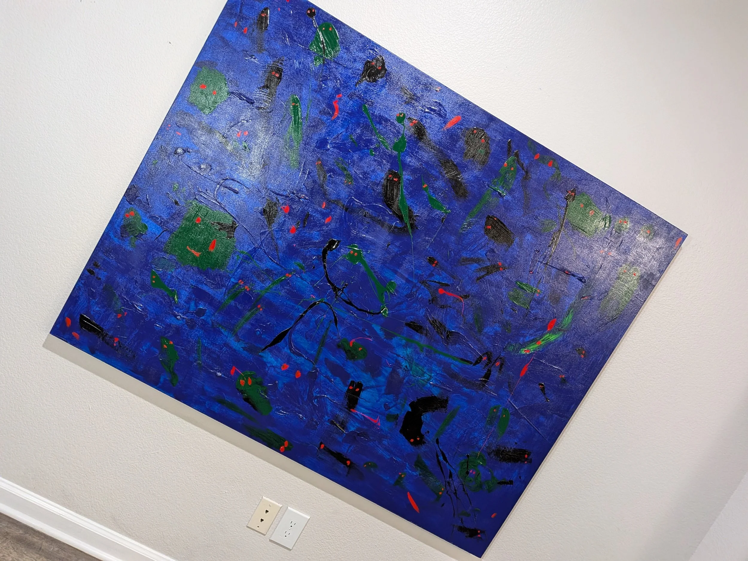 An abstract painting with a predominantly blue background, featuring black, green, and red splatters and strokes, hanging on a white wall.