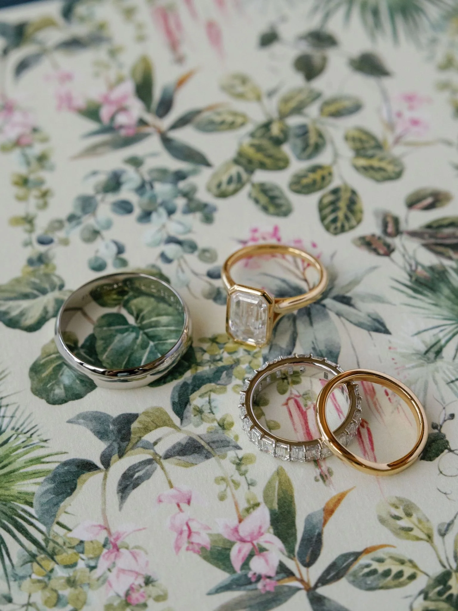Three rings placed on a floral tablecloth with green leaves and pink flowers.
