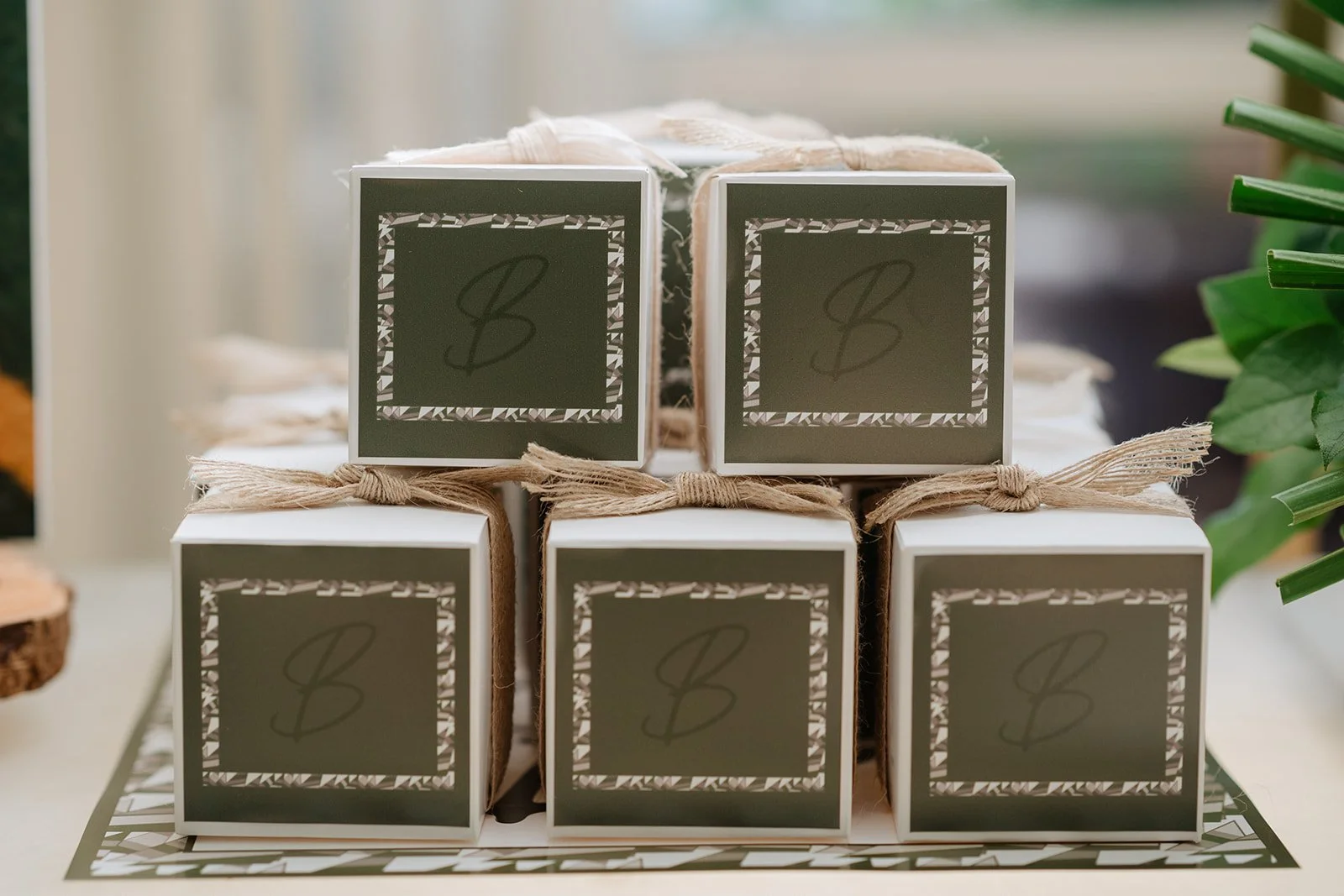 Stacks of small white boxes tied with twine, with labels featuring a stylized letter 'B' on a dark background with decorative border.