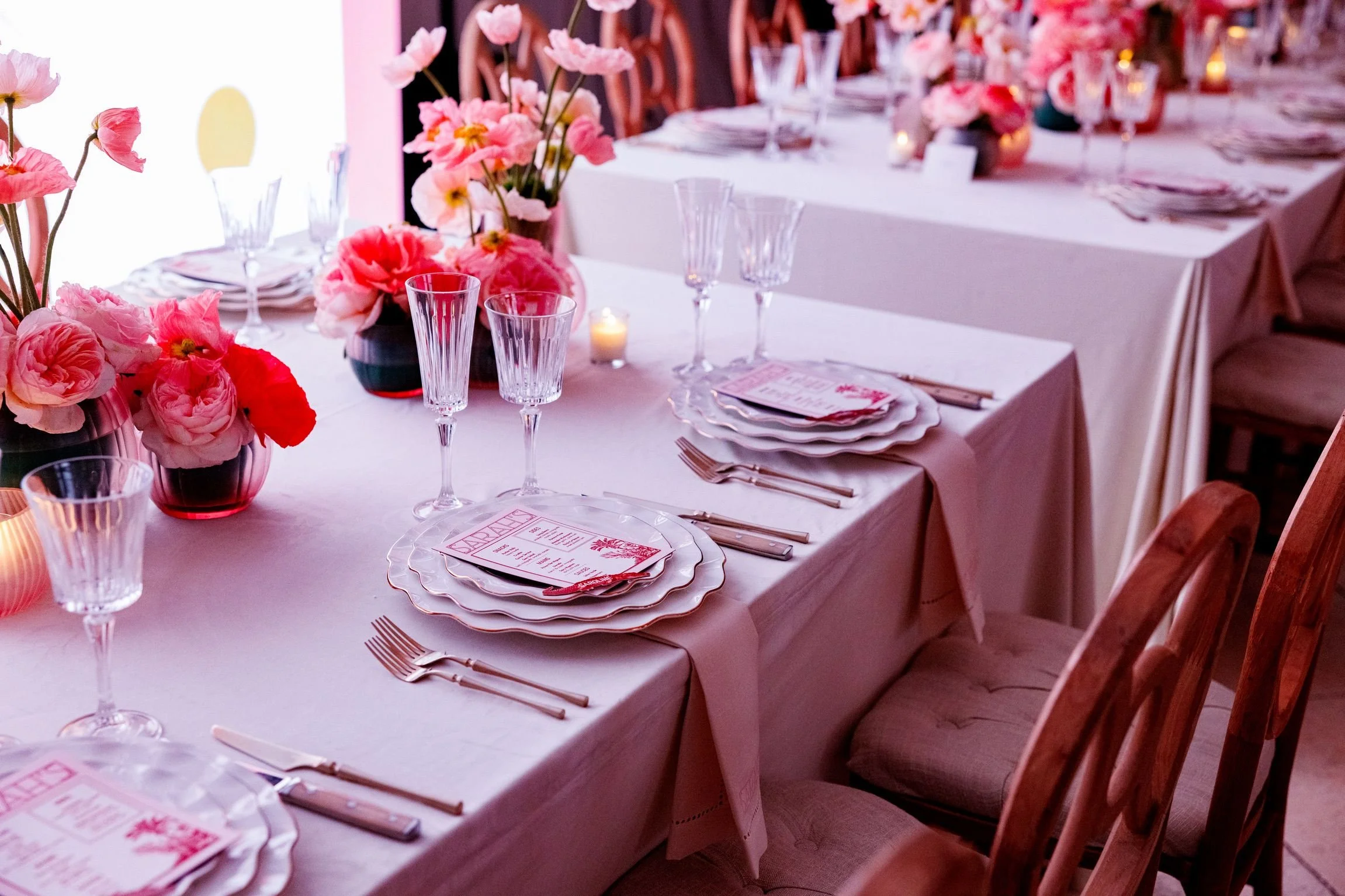 A dining table set for a celebration with pink flowers, candles, and glassware, featuring a pink themed centerpiece and place settings.