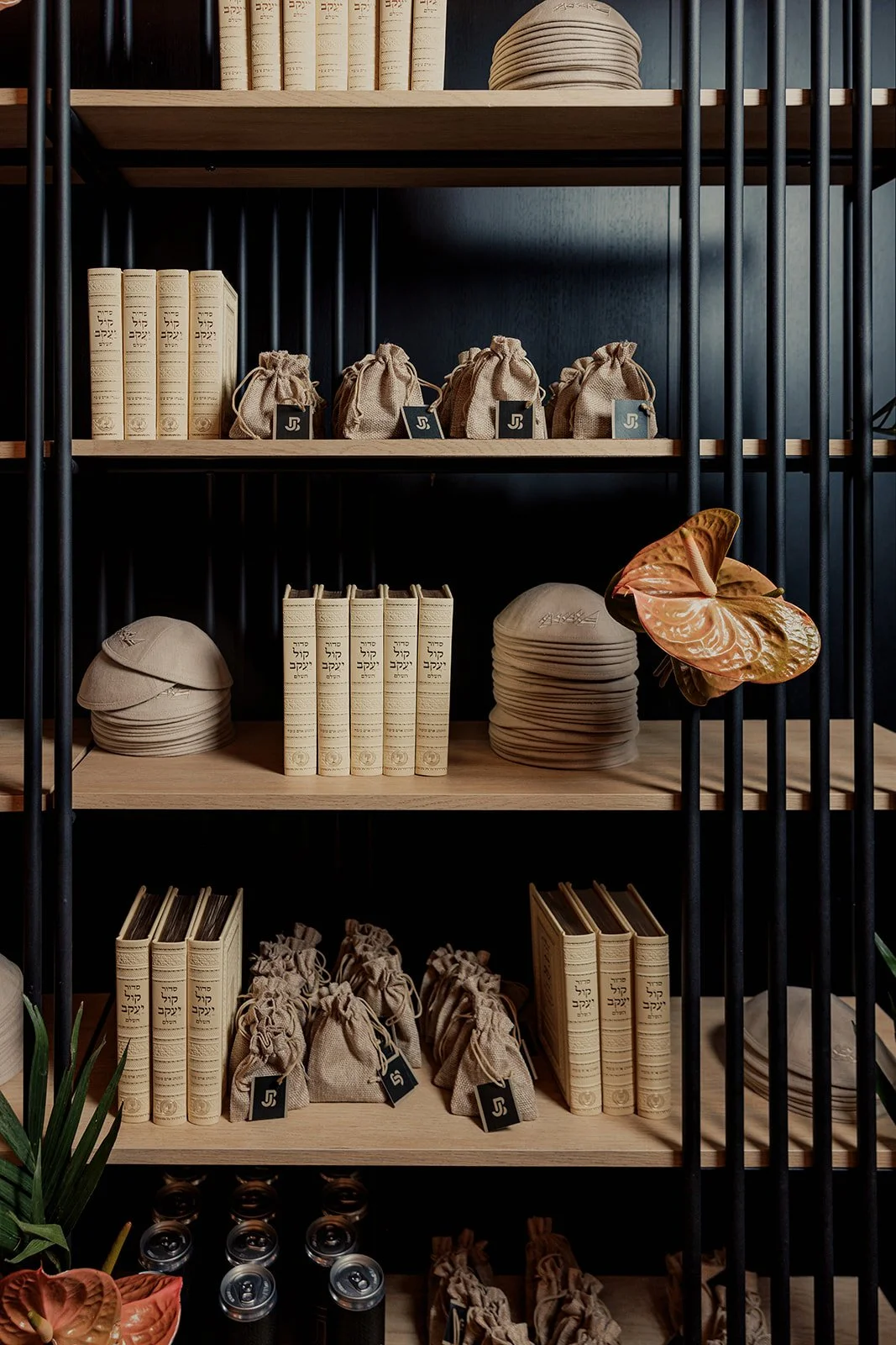 Wooden shelf divided into four sections, filled with books, small fabric bags, paper hats, and decorative items such as a large flower-shaped sculpture and native decor.
