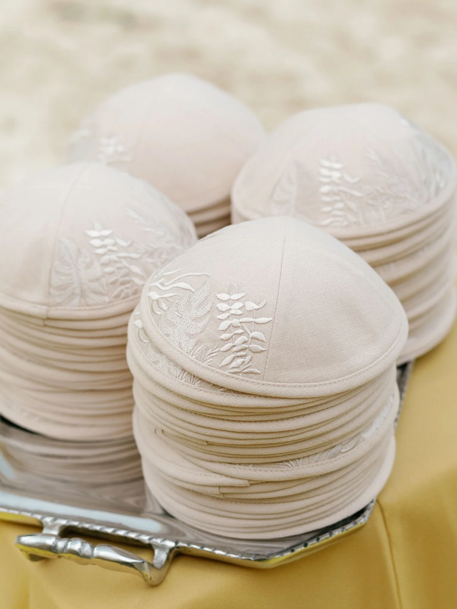 Stacked white Easter eggs with embossed floral patterns on a yellow surface, placed in a silver tray.