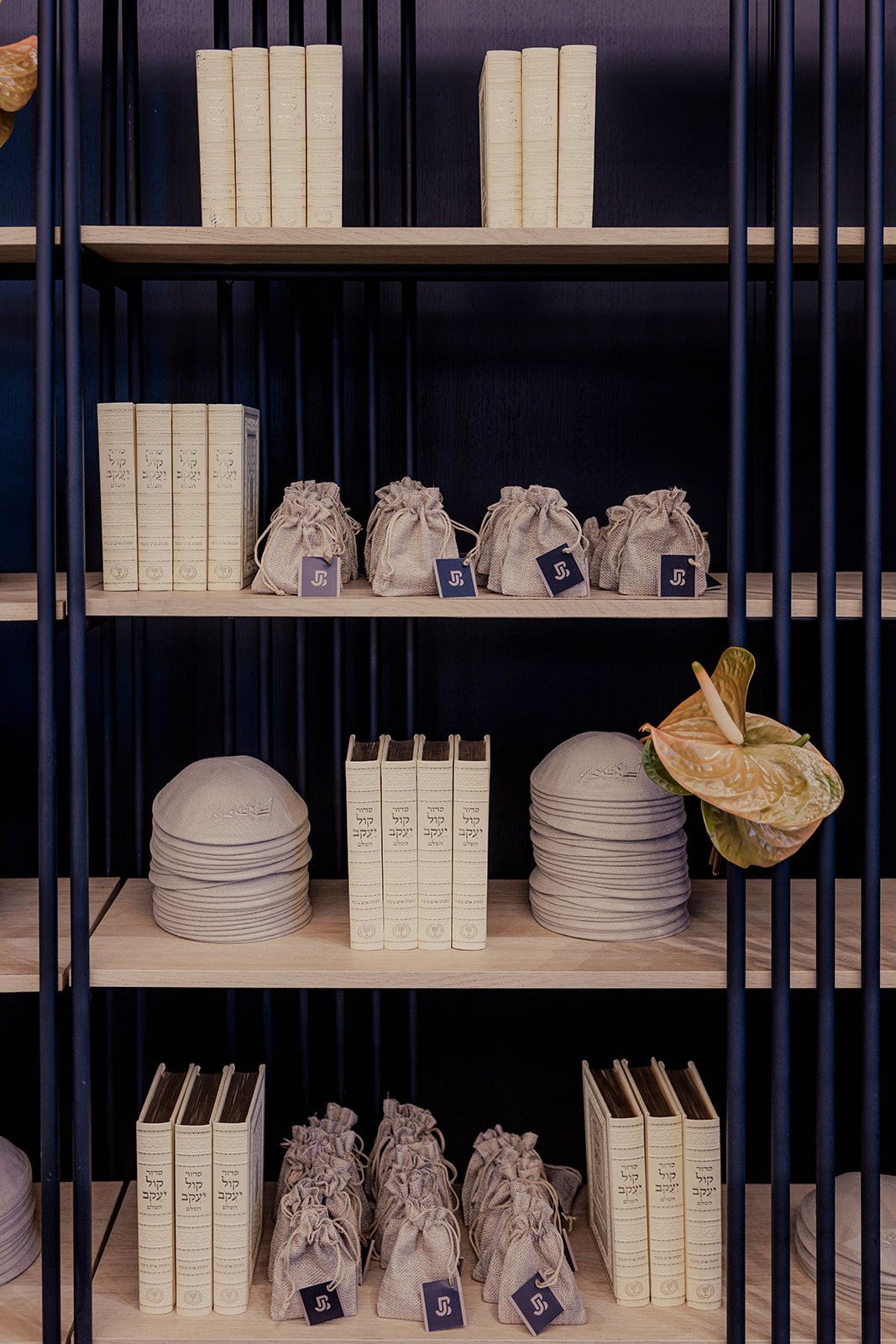 Books, small drawstring bags, and paper hats displayed on wooden shelves with a dark background.
