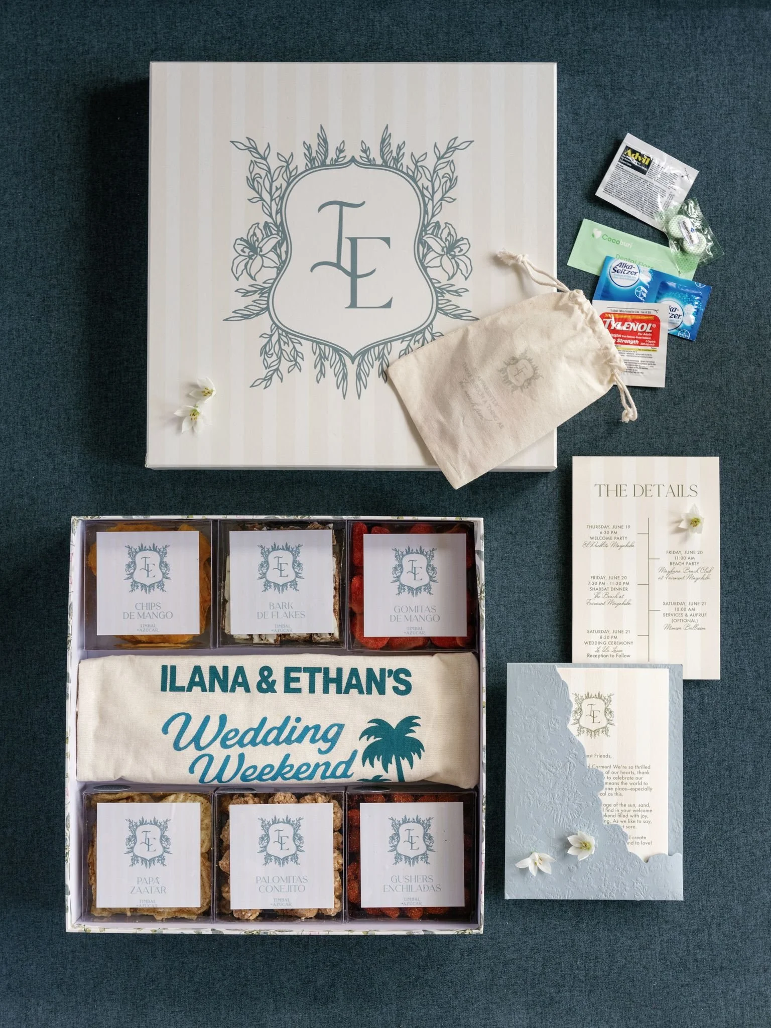 Wedding welcome bag with various candies and snacks, a personalized sign with the names Ilana and Ethan, wedding details, and decorative flowers.