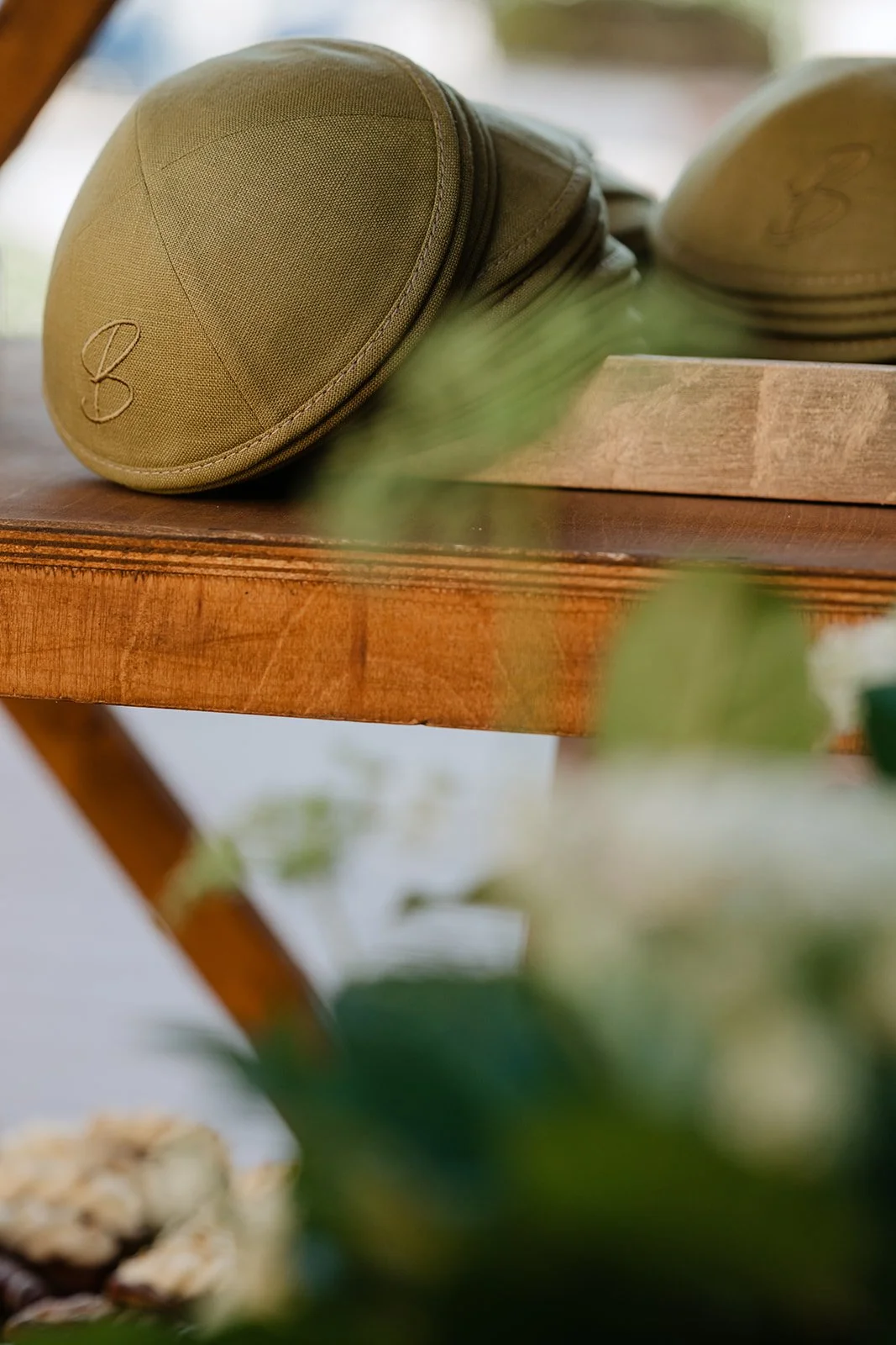 A close-up of two khaki-colored golf hats with a stitched 'B' logo, resting on a wooden table.