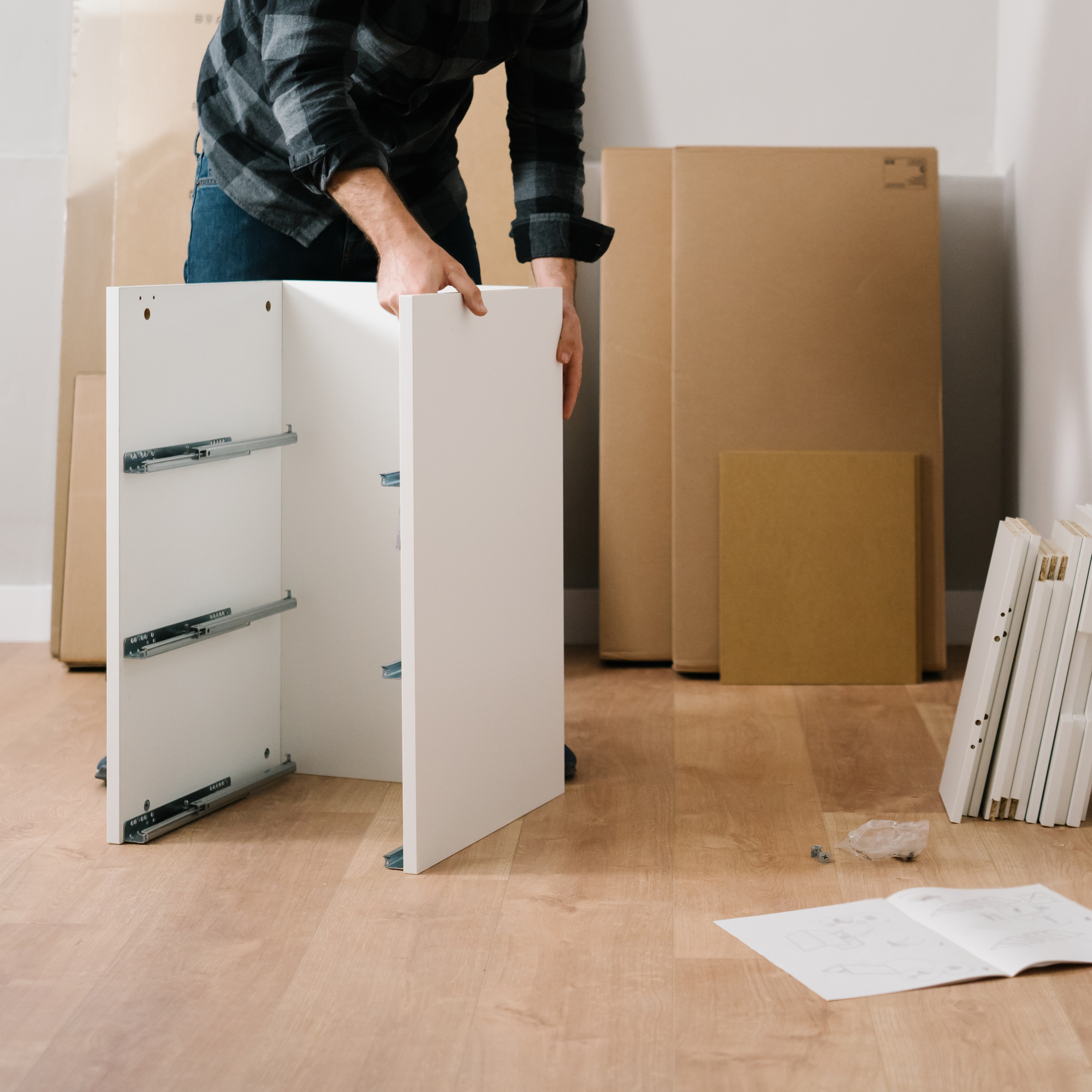 Person assembling furniture among cardboard boxes in a room with wooden flooring.