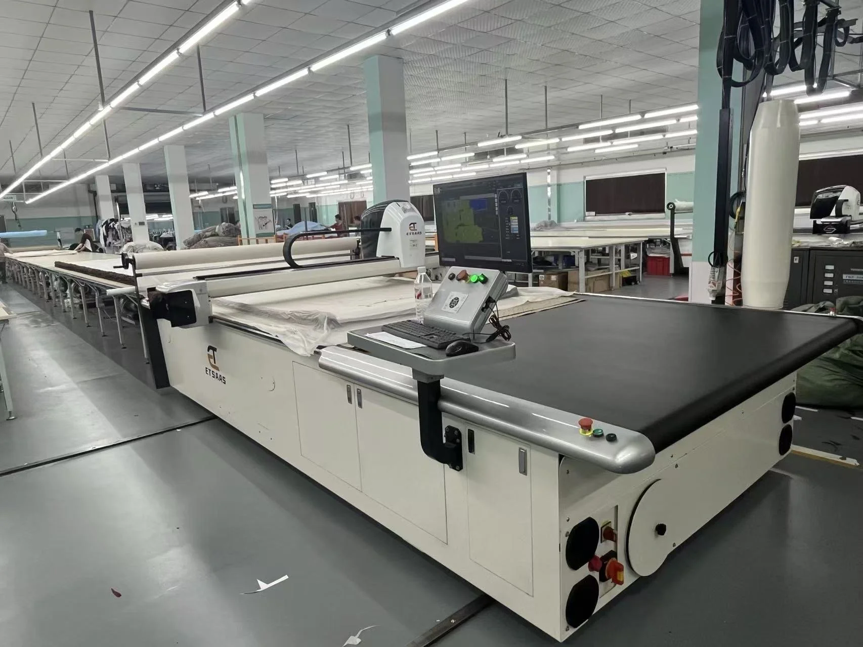 Industrial textile cutting machine in a factory setting with a computer monitor, keyboard, and mouse.