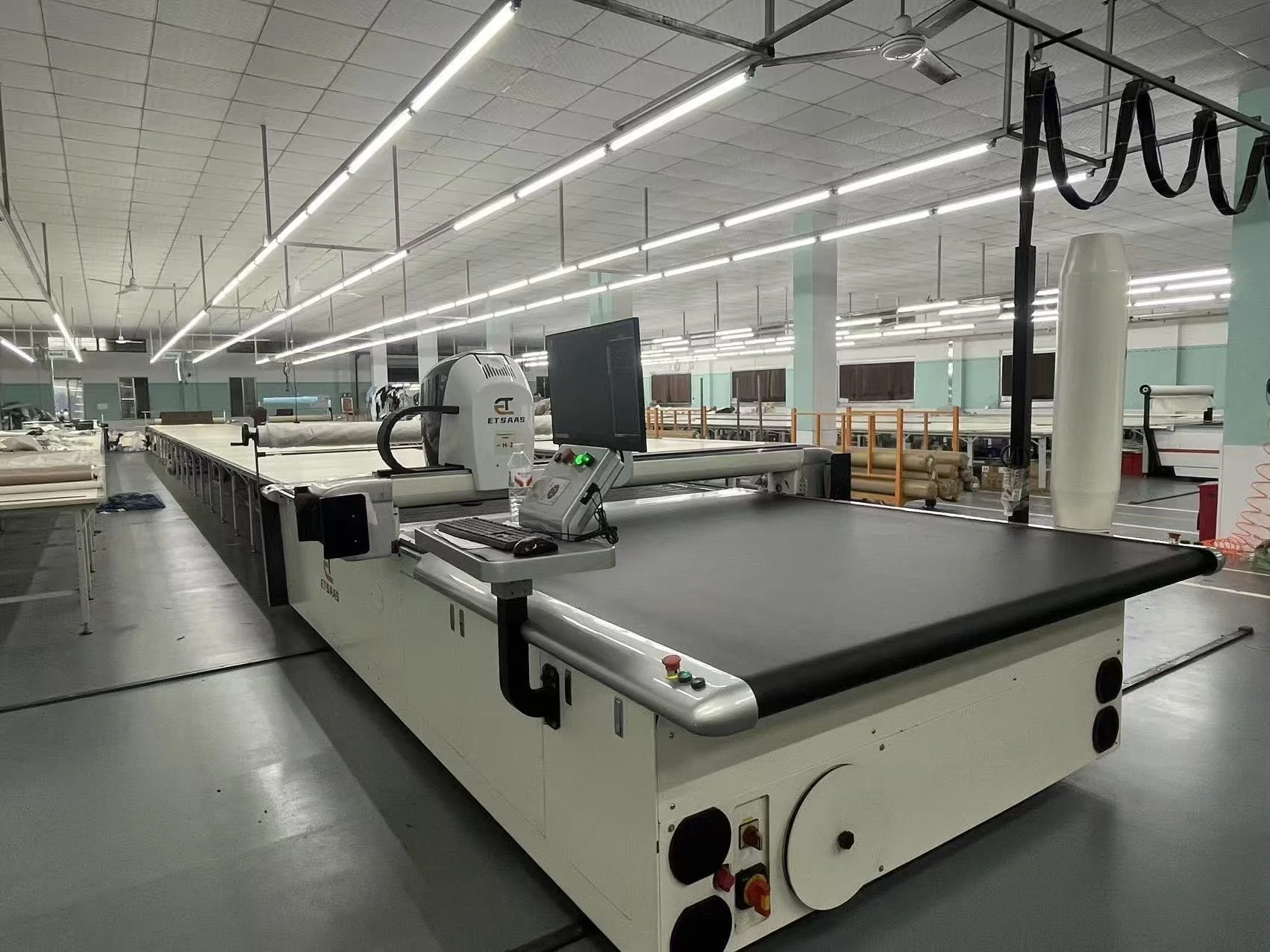 Large industrial fabric cutting machine in a spacious factory with bright overhead lighting and neatly organized materials in the background.