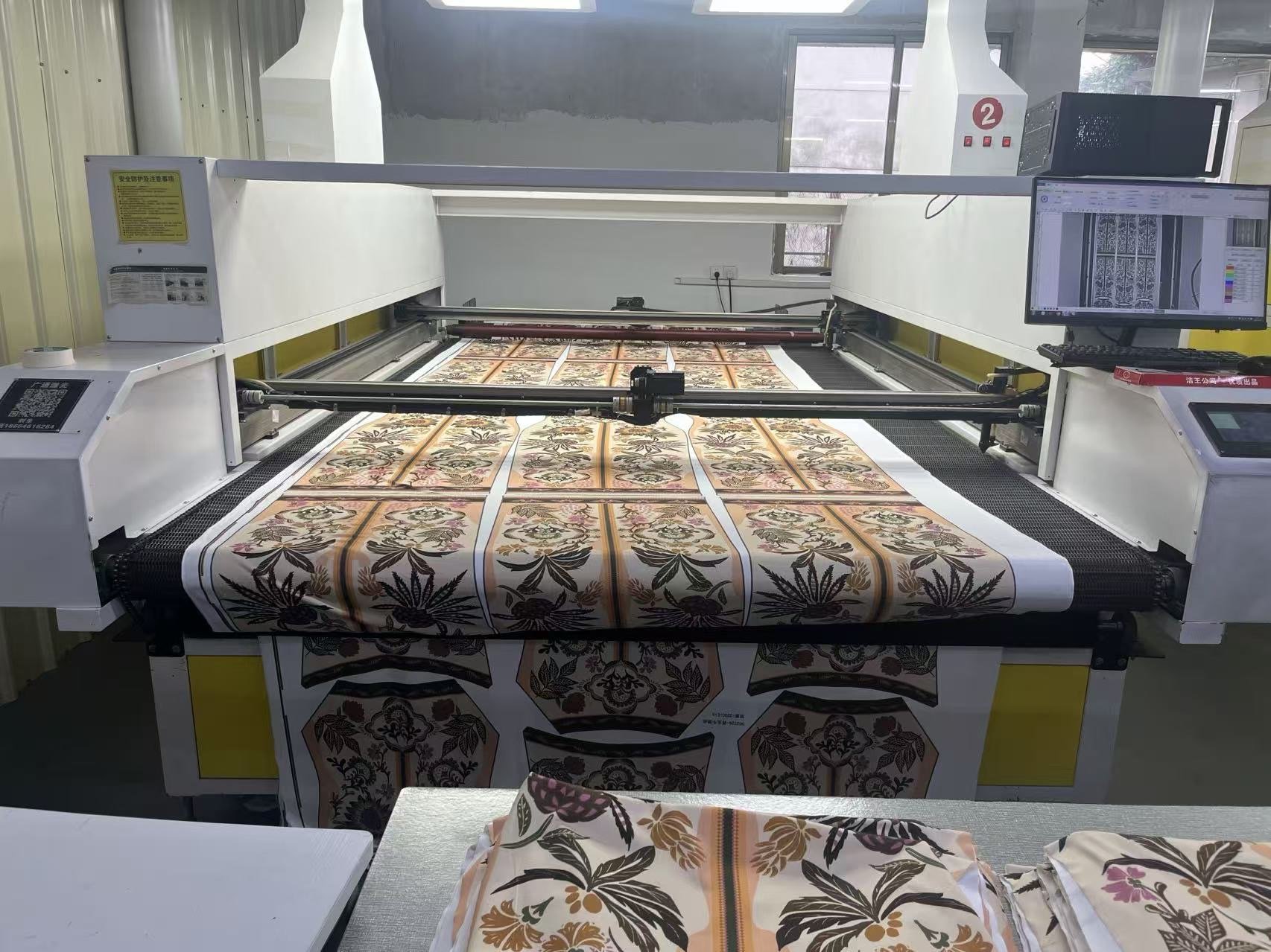 A large textile printing machine producing fabric with floral patterns in shades of brown, beige, and pink.