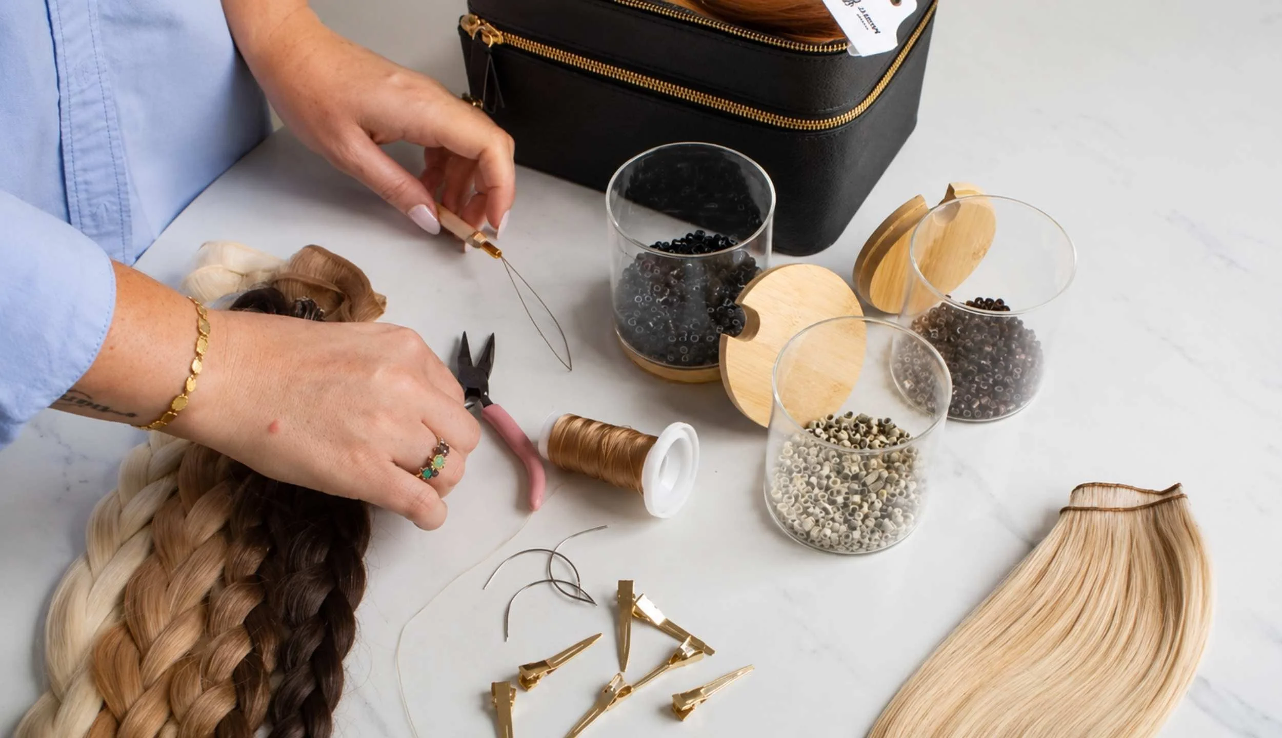 A person braiding hair with various beads, hair clips, and hairpieces on a white table.
