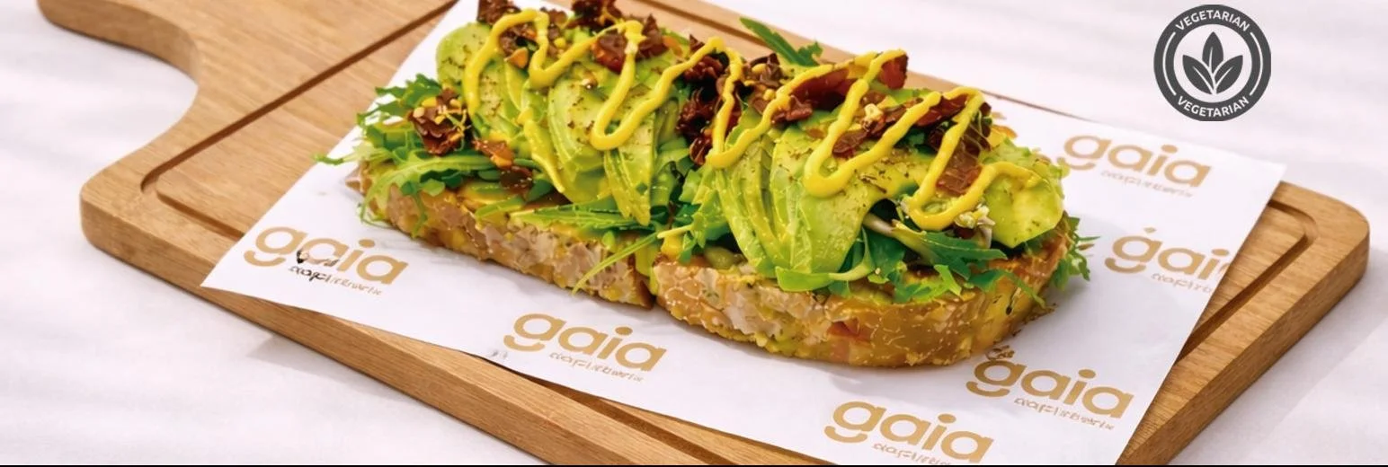 Tarta vegetariana con aguacate, verduras y salsa en un plato sobre una tabla de madera, con logo de Gaia en papel decorativo y sello vegetal en la esquina superior derecha.