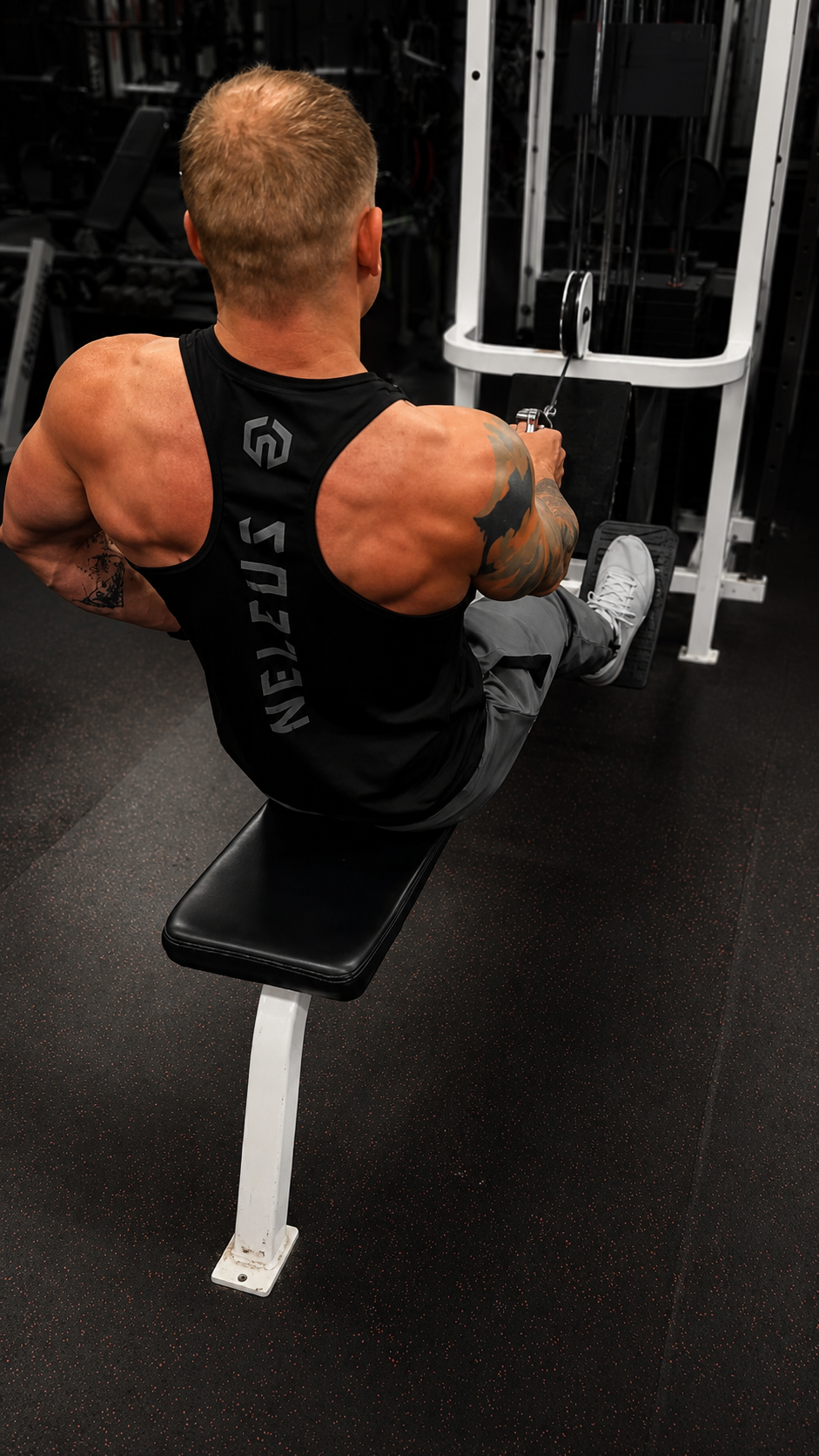 Man with muscular arms and tattoos using a rowing machine at the gym.