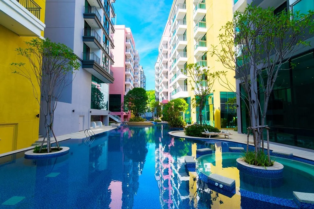 Colorful apartment buildings surrounding a pool with lounge chairs and trees.