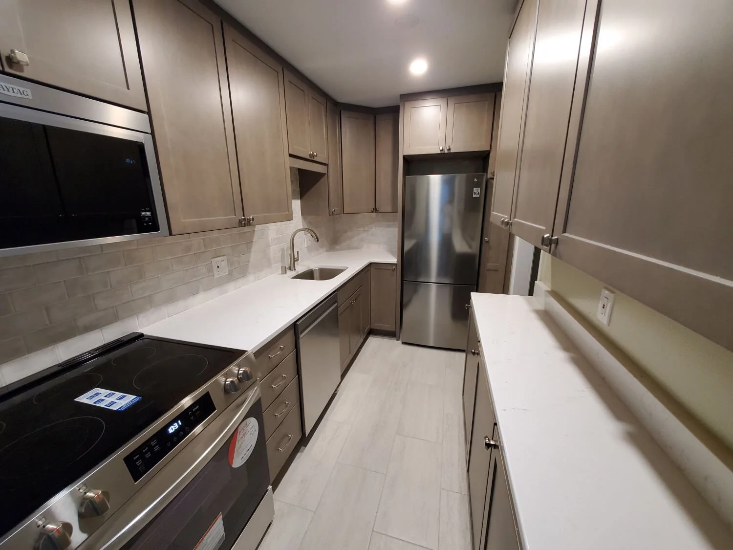 Modern kitchen with light brown cabinets, white countertops, stainless steel appliances including a refrigerator and stove, and beige tile backsplash.