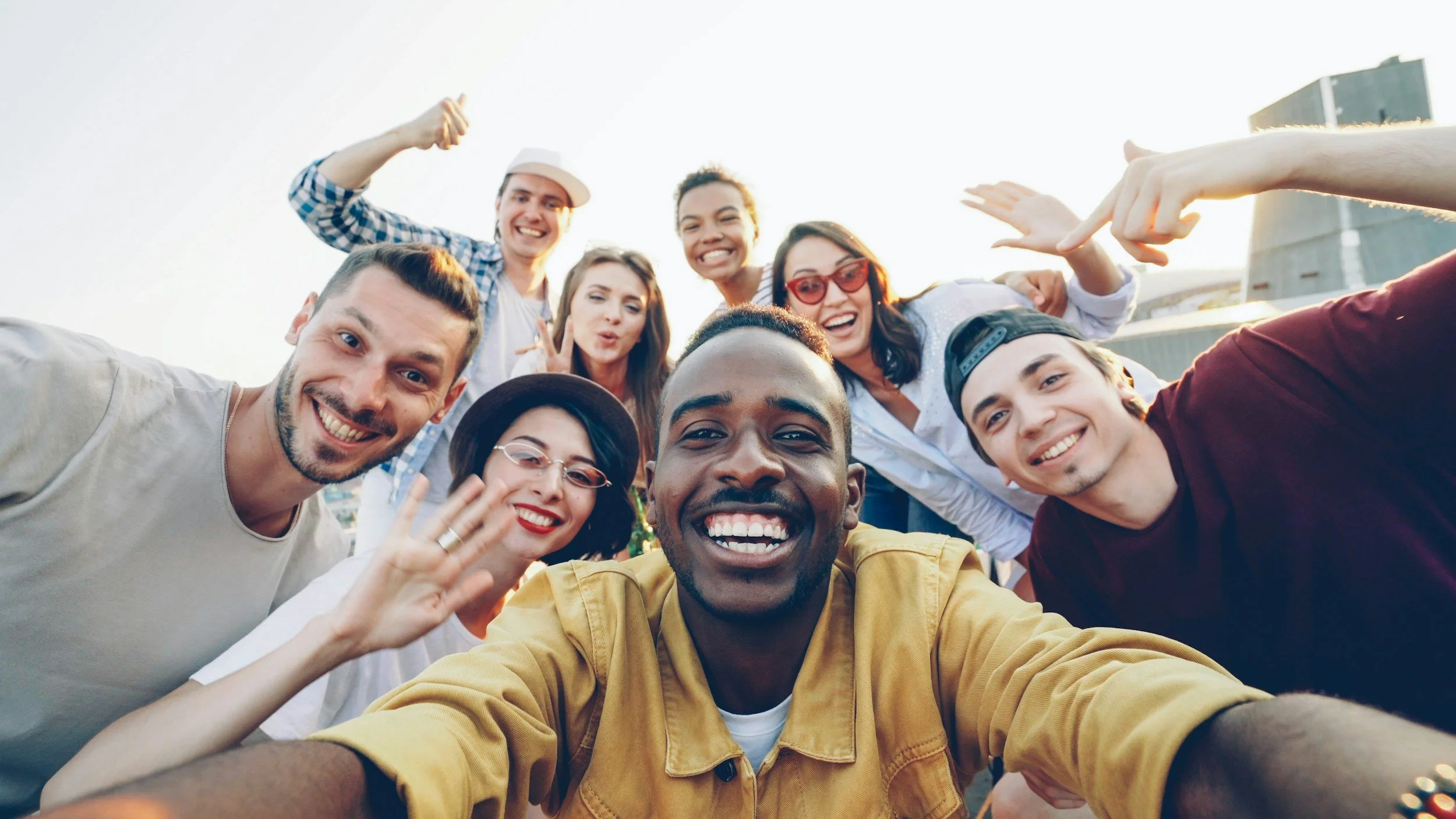 A group of smiling friends taking a selfie outdoors during sunset.