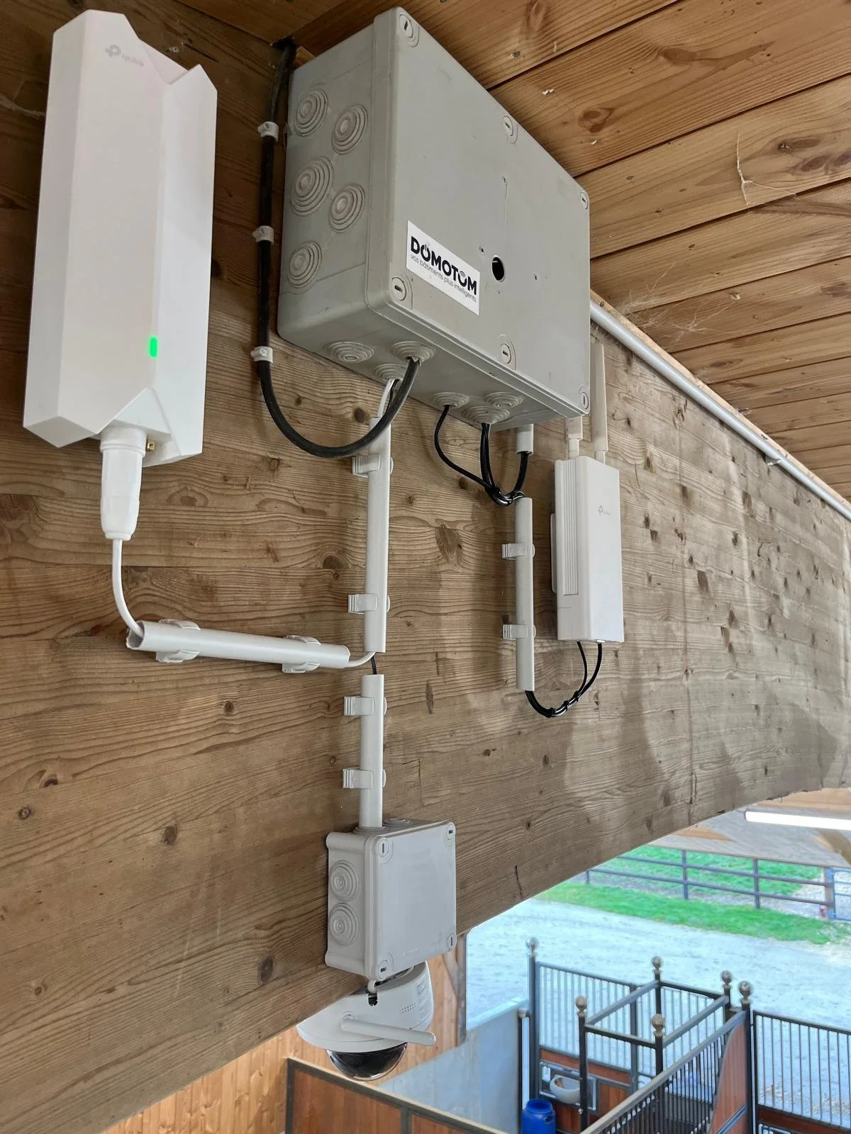 Un tableau de bord de systèmes de sécurité comprenant un panneau de contrôle, une caméra, des boîtes de connexion, et un panneau de réseau, fixés sur un mur en bois.