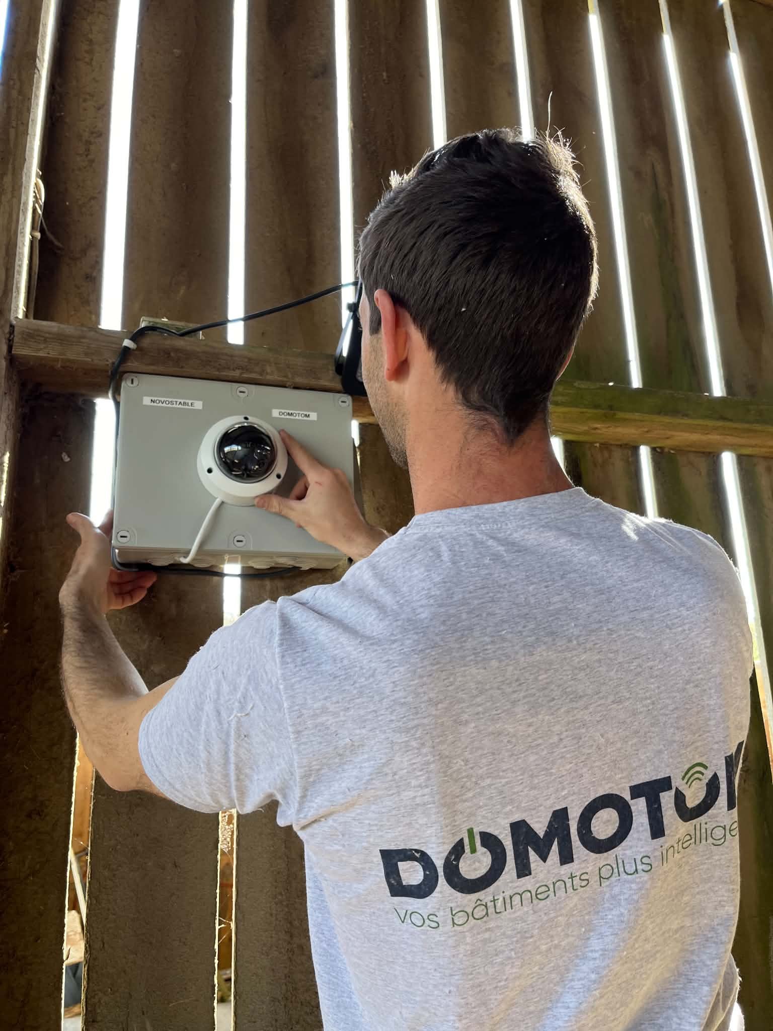 Un homme en train d'installer une caméra de surveillance montée sur un mur en bois.
