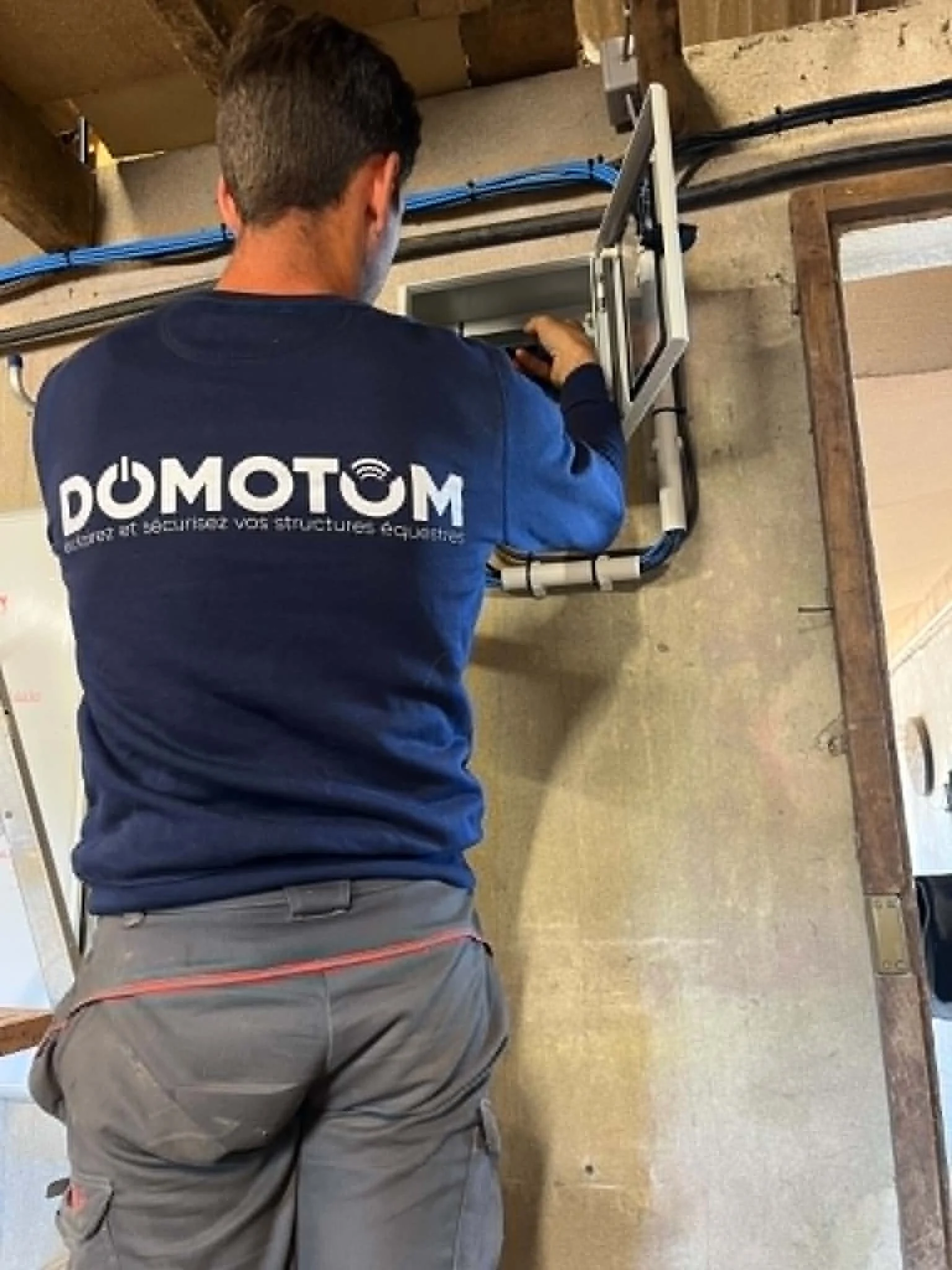 Quelqu'un de chez Domotom en train de travailler sur un tableau électrique ou un panneau de distribution électrique dans un intérieur en bois.