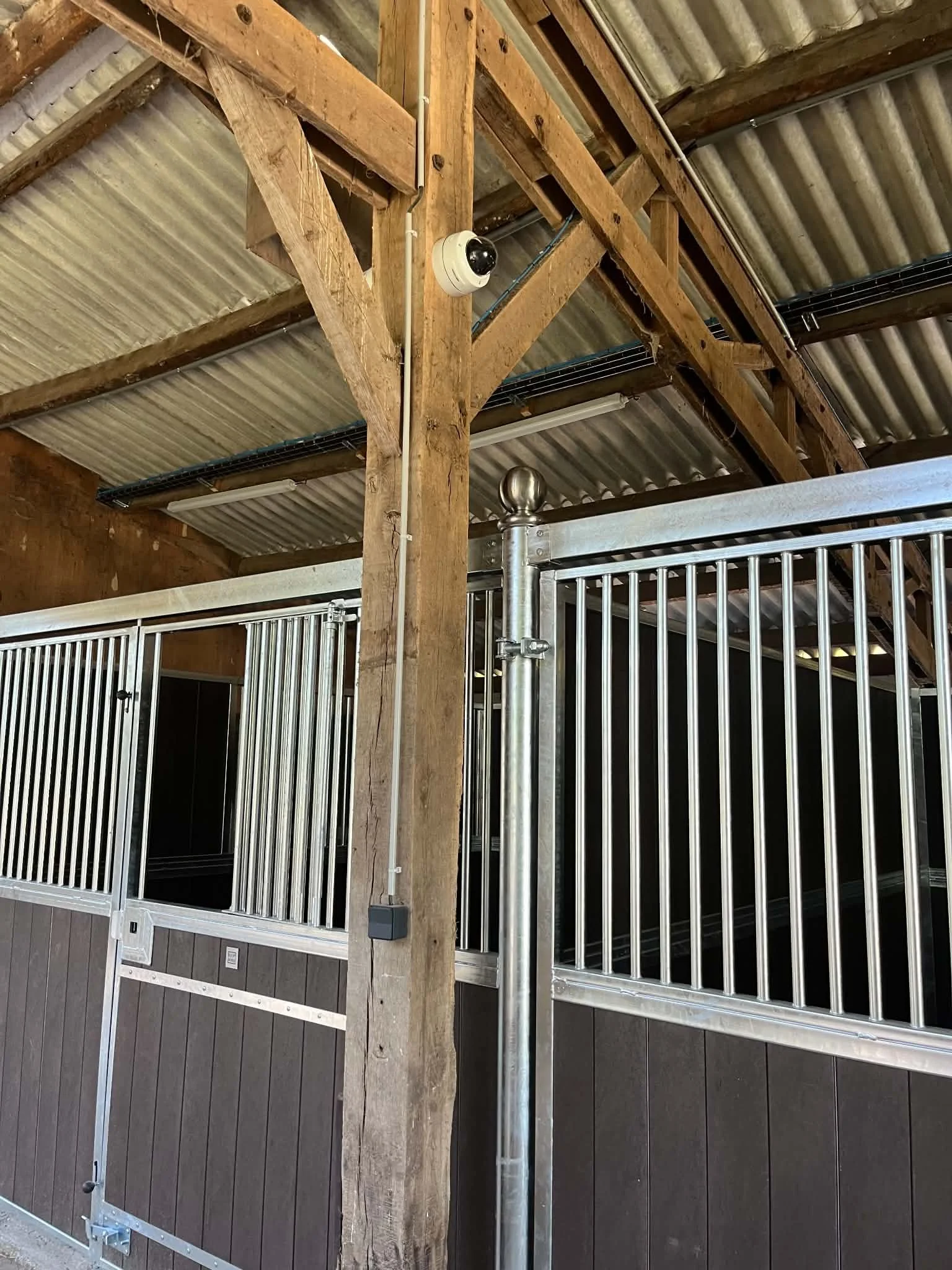 Ecurie avec caméra de vidéosurveillance discrète installée sur un poteau en bois pour surveiller un boxe à cheval.