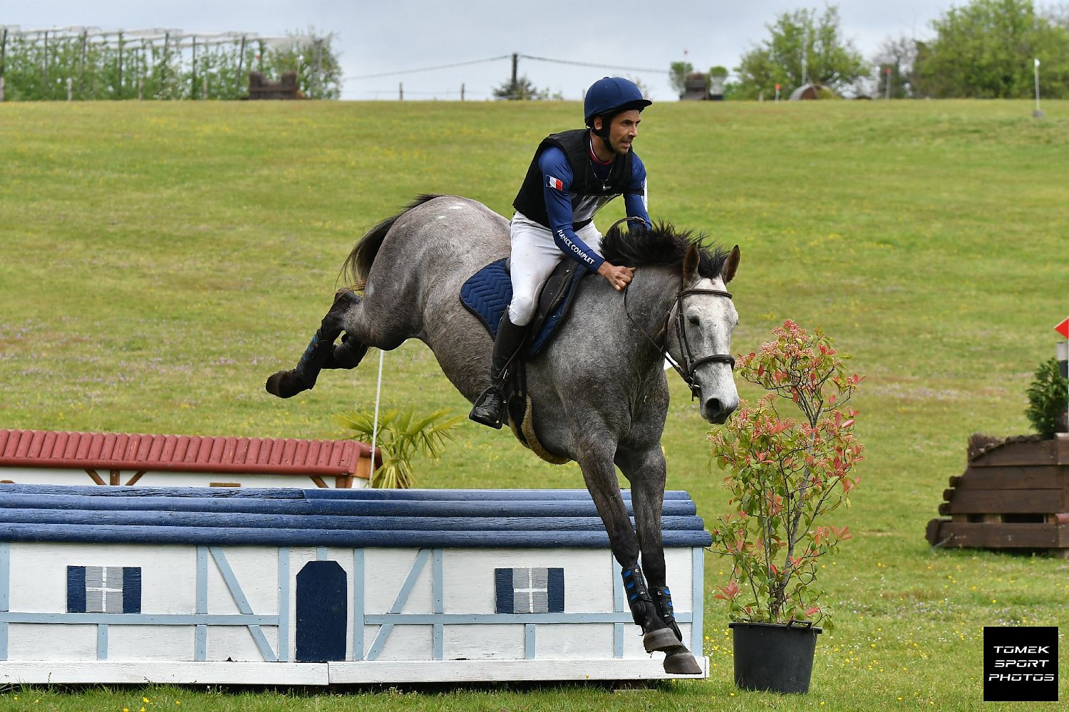 Un cavalier en tenue de compétition sautant un obstacle lors d'un cross en concours complet.
