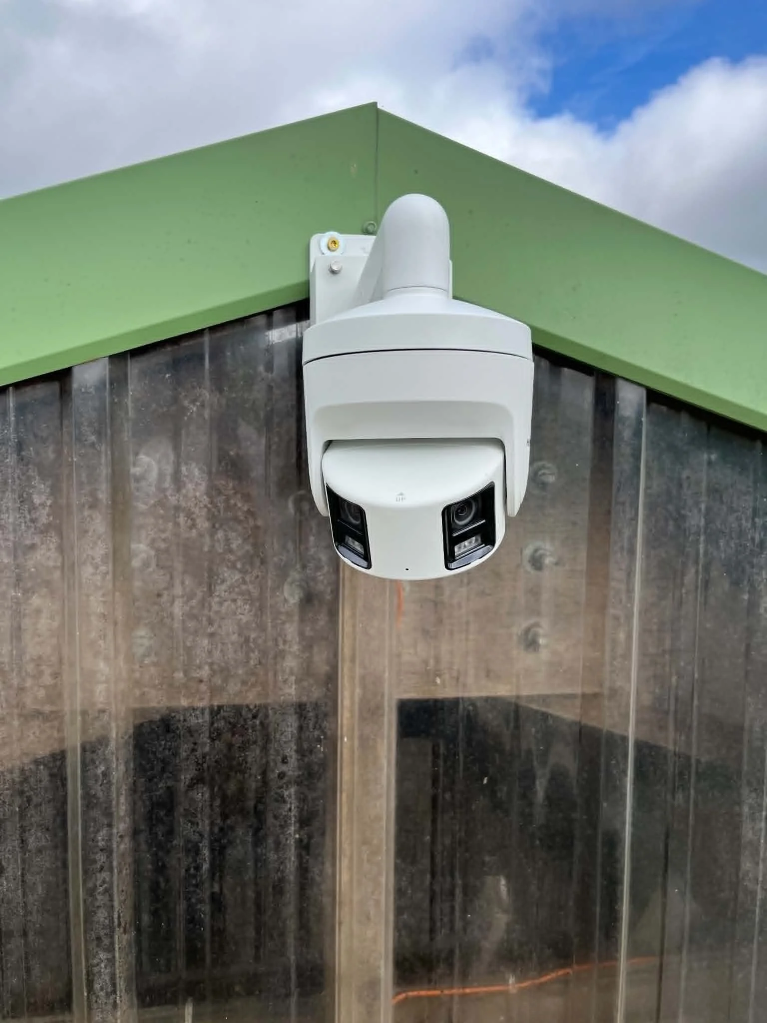Caméra de surveillance 180° installé sur une ferme sous un toit vert avec un ciel bleu en arrière-plan.