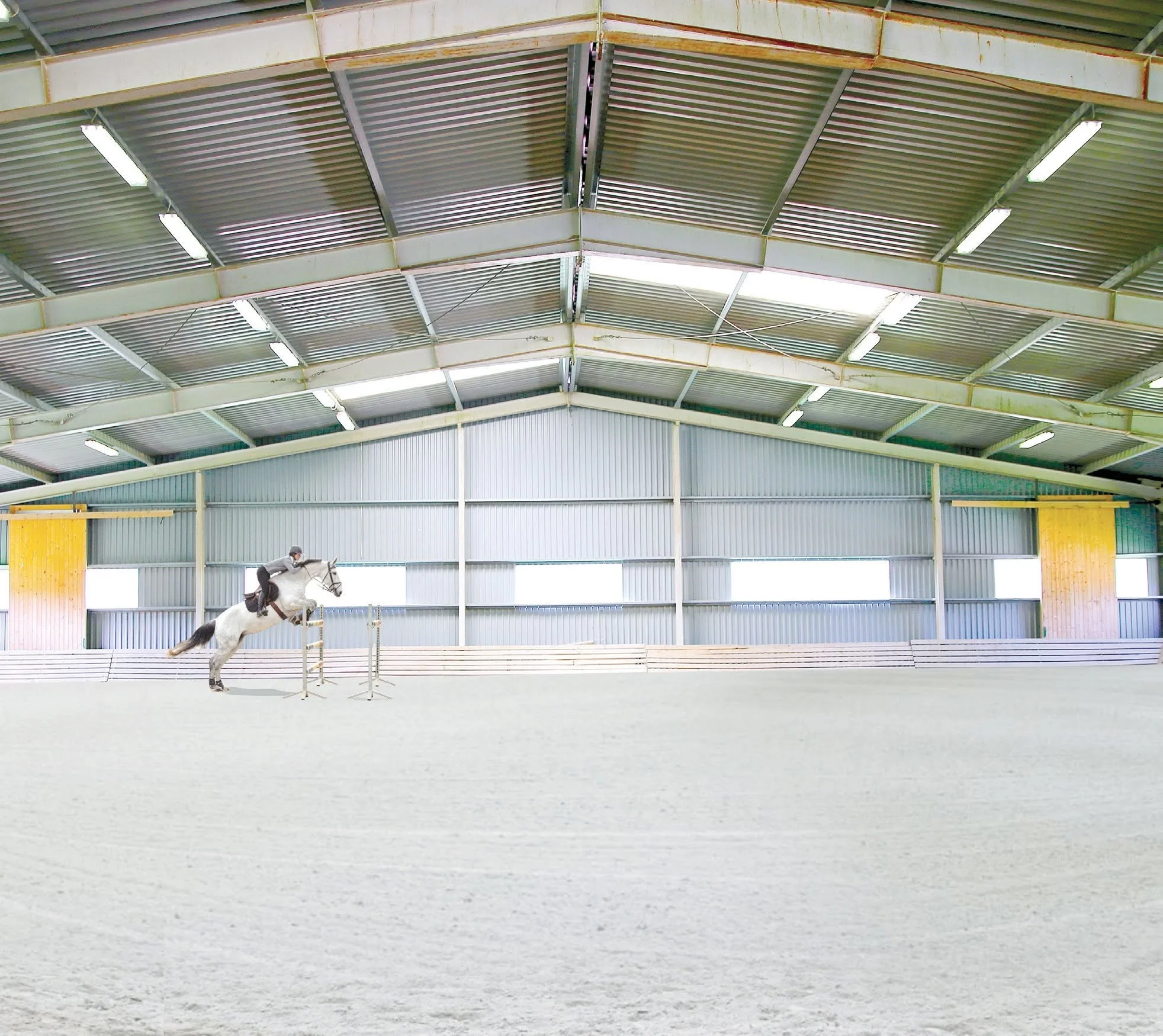 Un manège équestre intérieur avec un cheval blanc sautant un obstacle, cela sous un éclairage parfait.