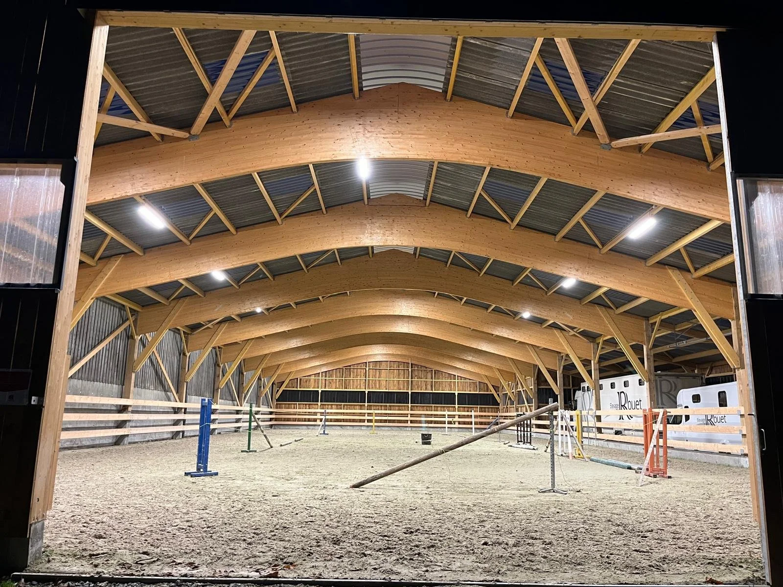 Intérieur d'un manège équestre en construction avec une structure en bois et un sol en sable.