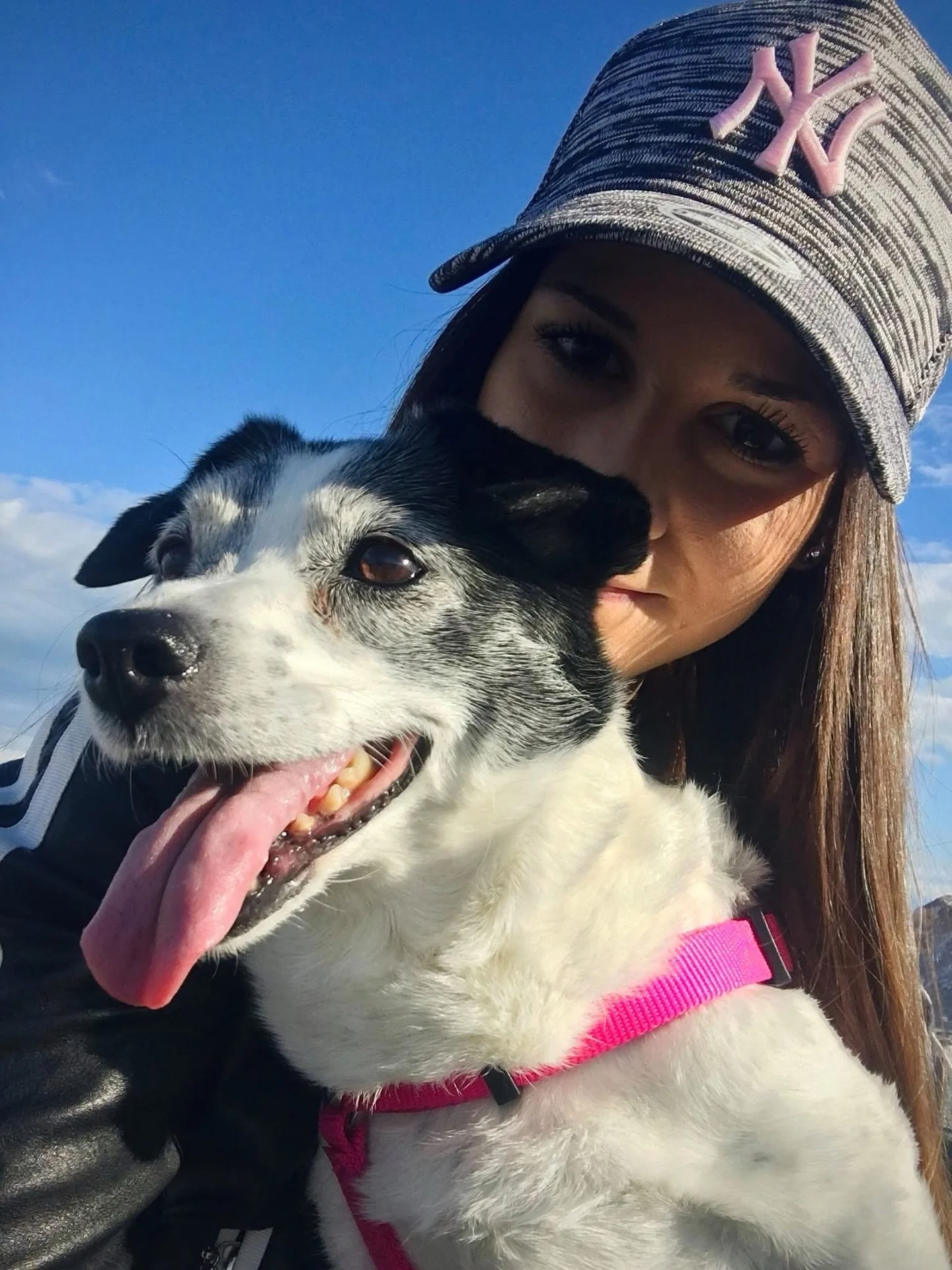 Una donna con cappellino e cane bianco e nero fuori in un cielo blu.