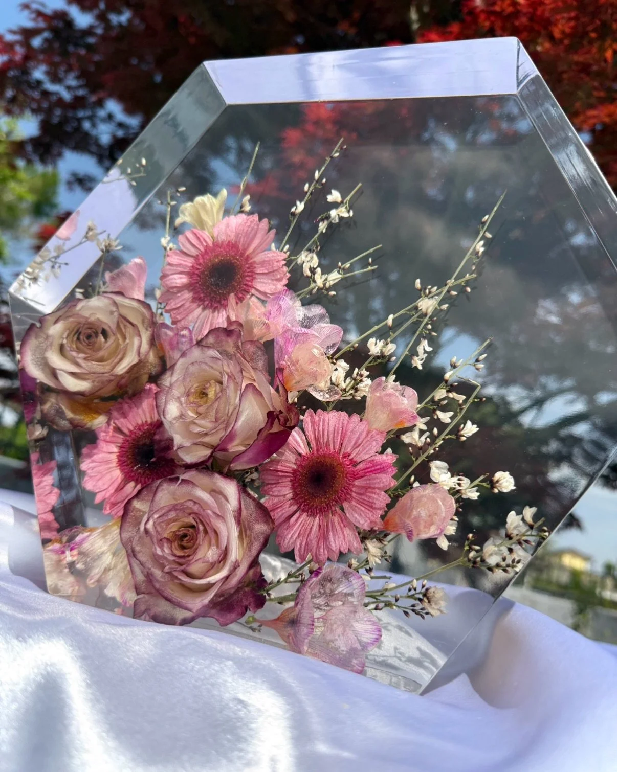 Creazione in resina di fiori misti con rose, margherite rosa e fiorellini bianchi, con sfondo di alberi autunnali.