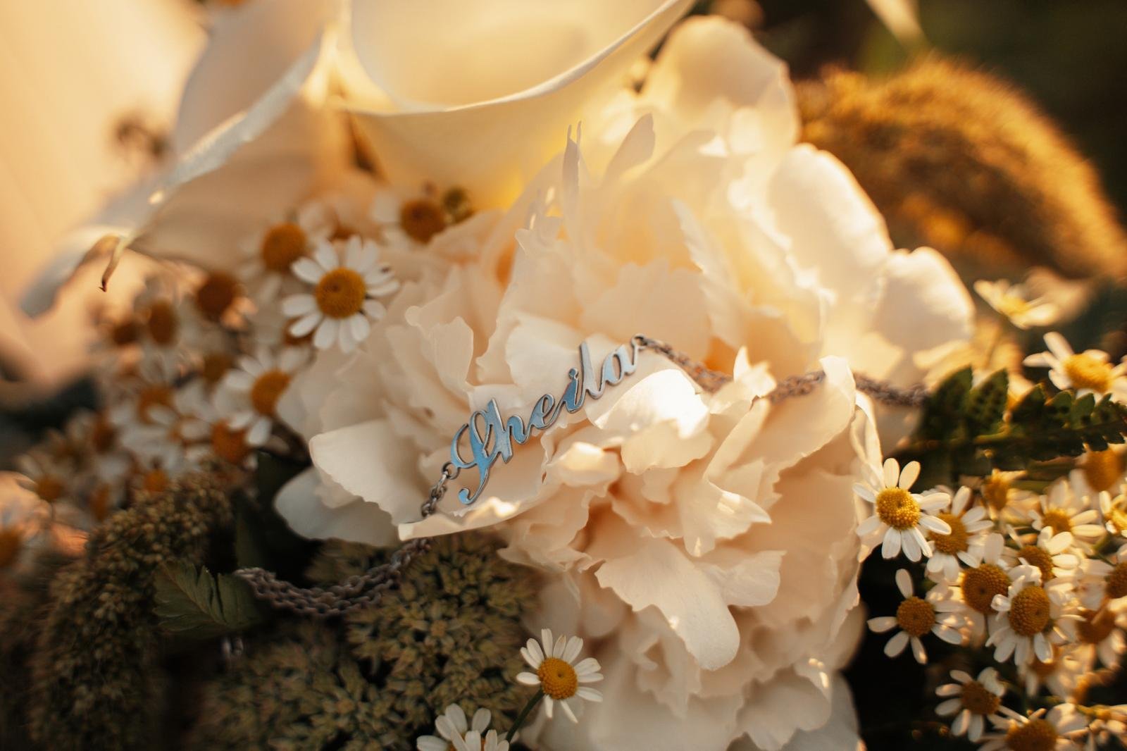 Composizione floreale con peonie bianche, margherite e altri fiori selvatici, decorata con una catena e una parola 'Ginevra' in metallo