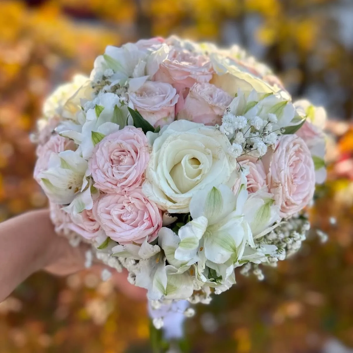 Mazzo di fiori con rose bianche e rosa, gigli bianchi e piccole fioriture bianche, tenuto da una mano.