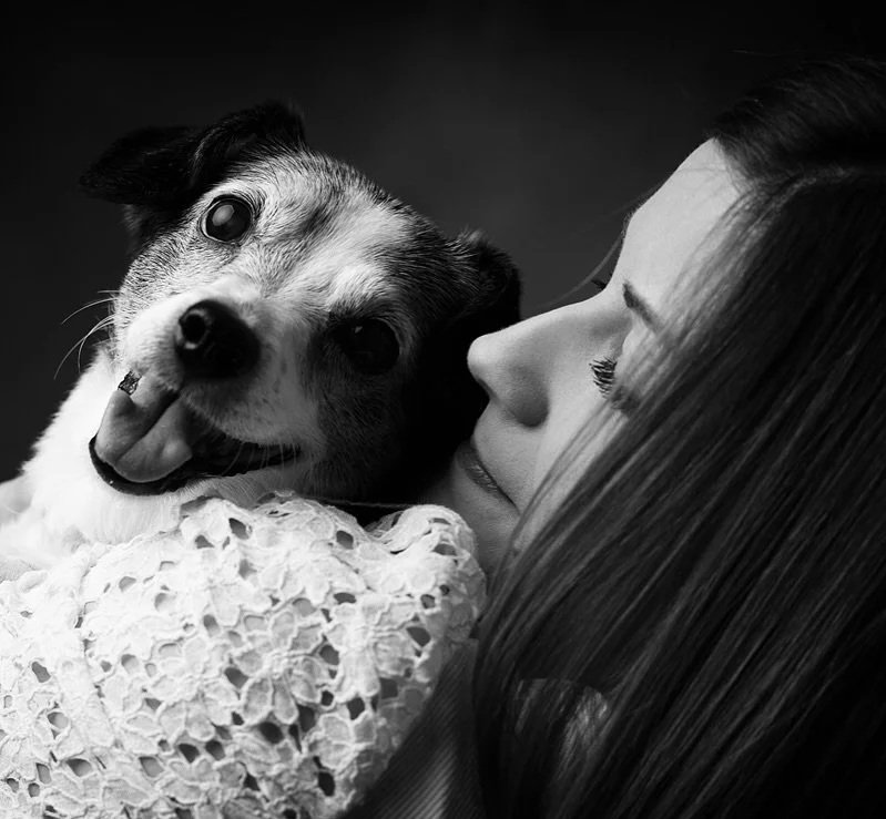 Una donna abbraccia un cane, entrambi sorridenti, in una foto in bianco e nero.
