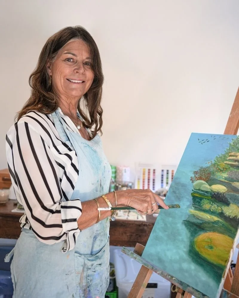 Janet Morris in her home studio in Port Douglas, Far North Queensland. Pictured while painting a landscape on a canvas set on an easel.