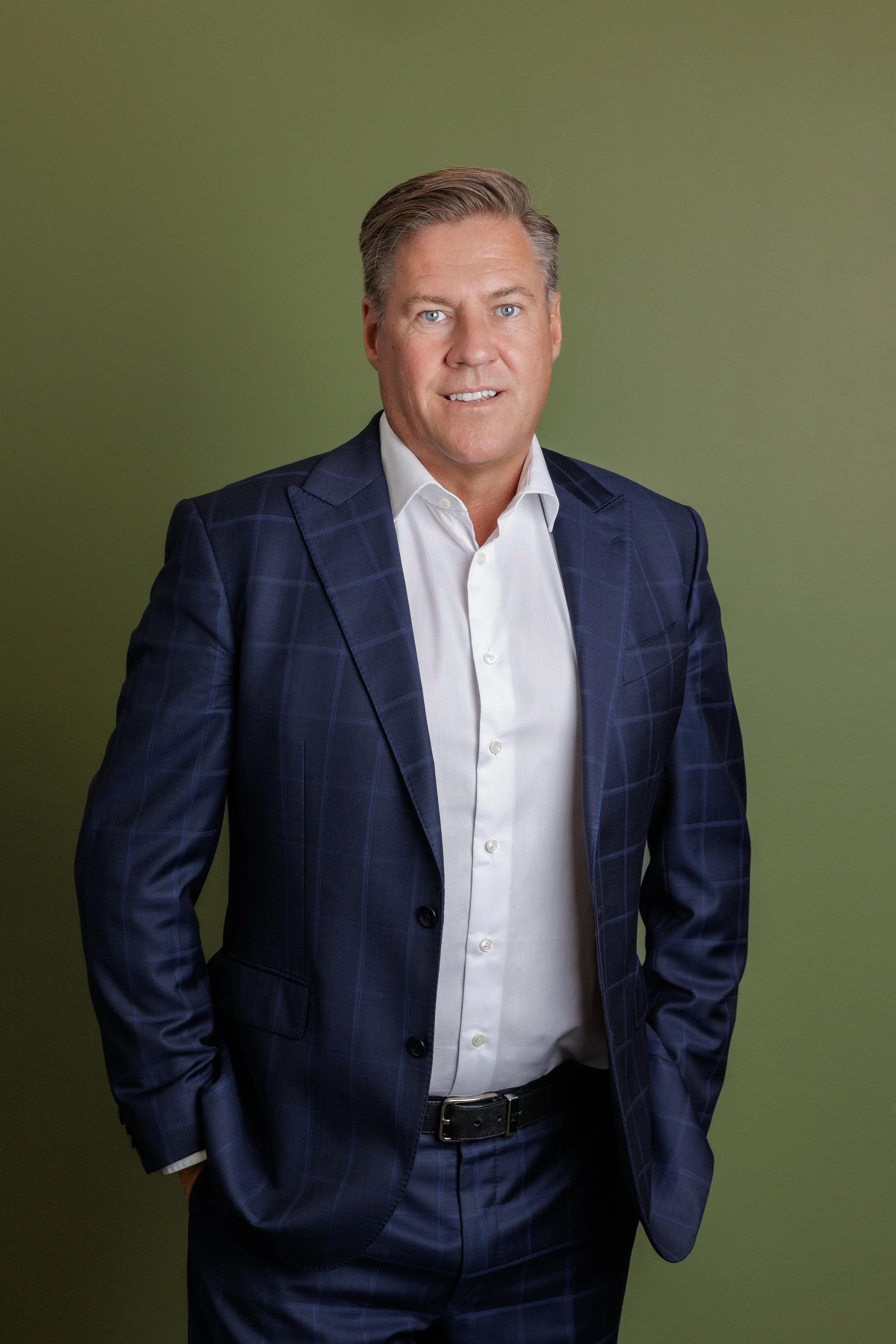 Professional man in a navy checkered suit and white shirt standing against a green background.