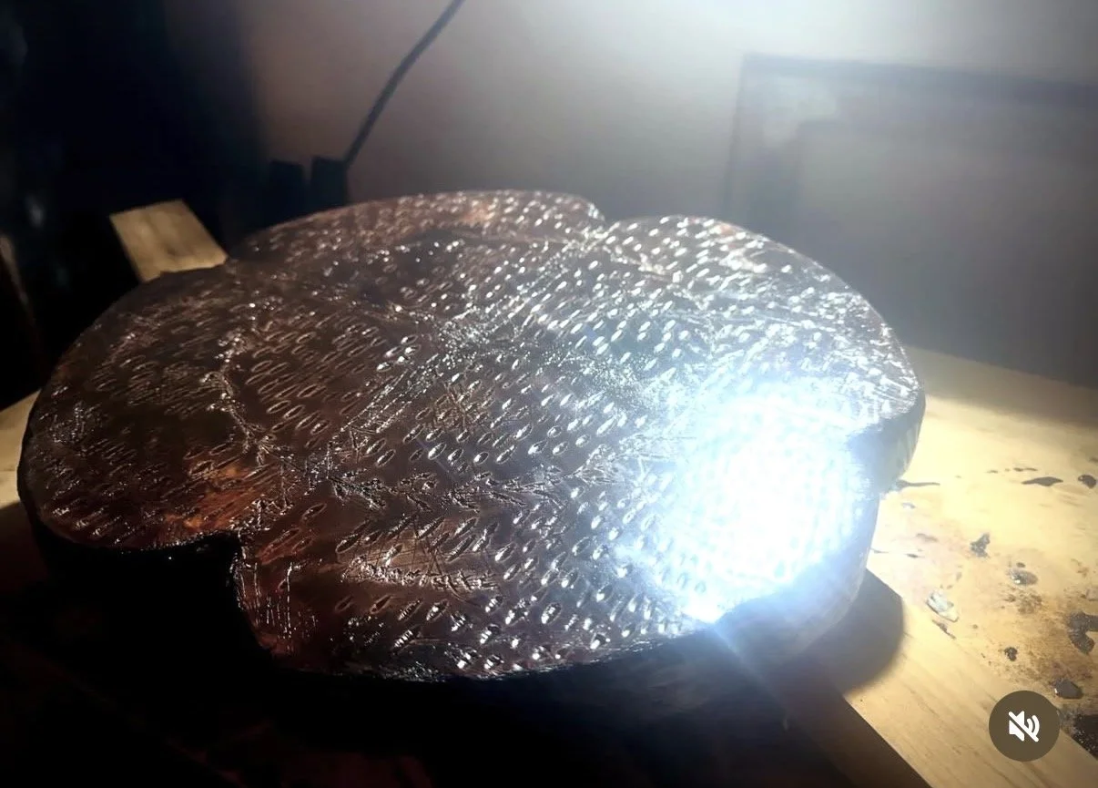A carved wooden object illuminated by a bright light on a wooden surface.