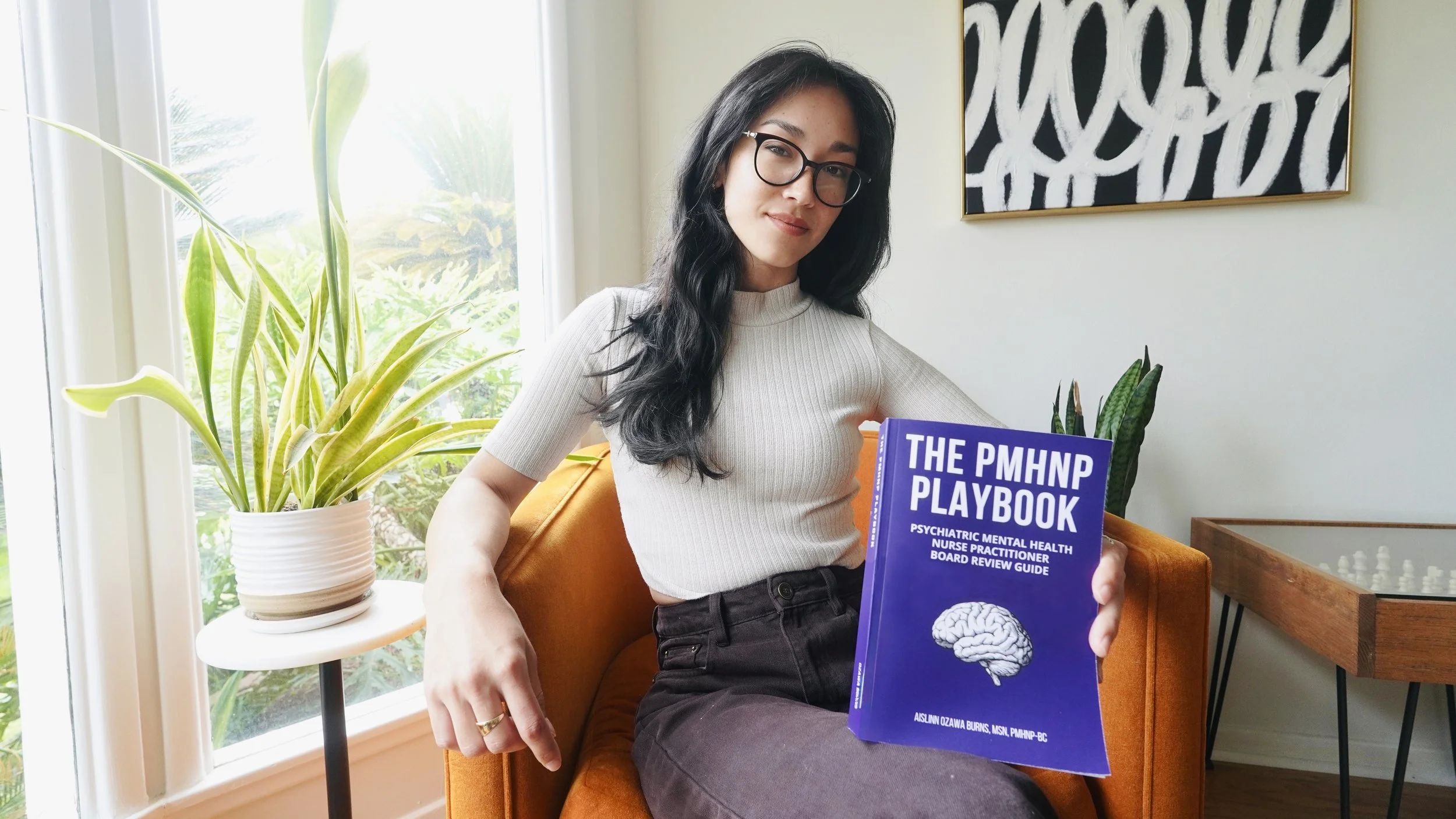PMHNP student and author holding The PMHNP Playbook psychiatric mental health nurse practitioner board review book.