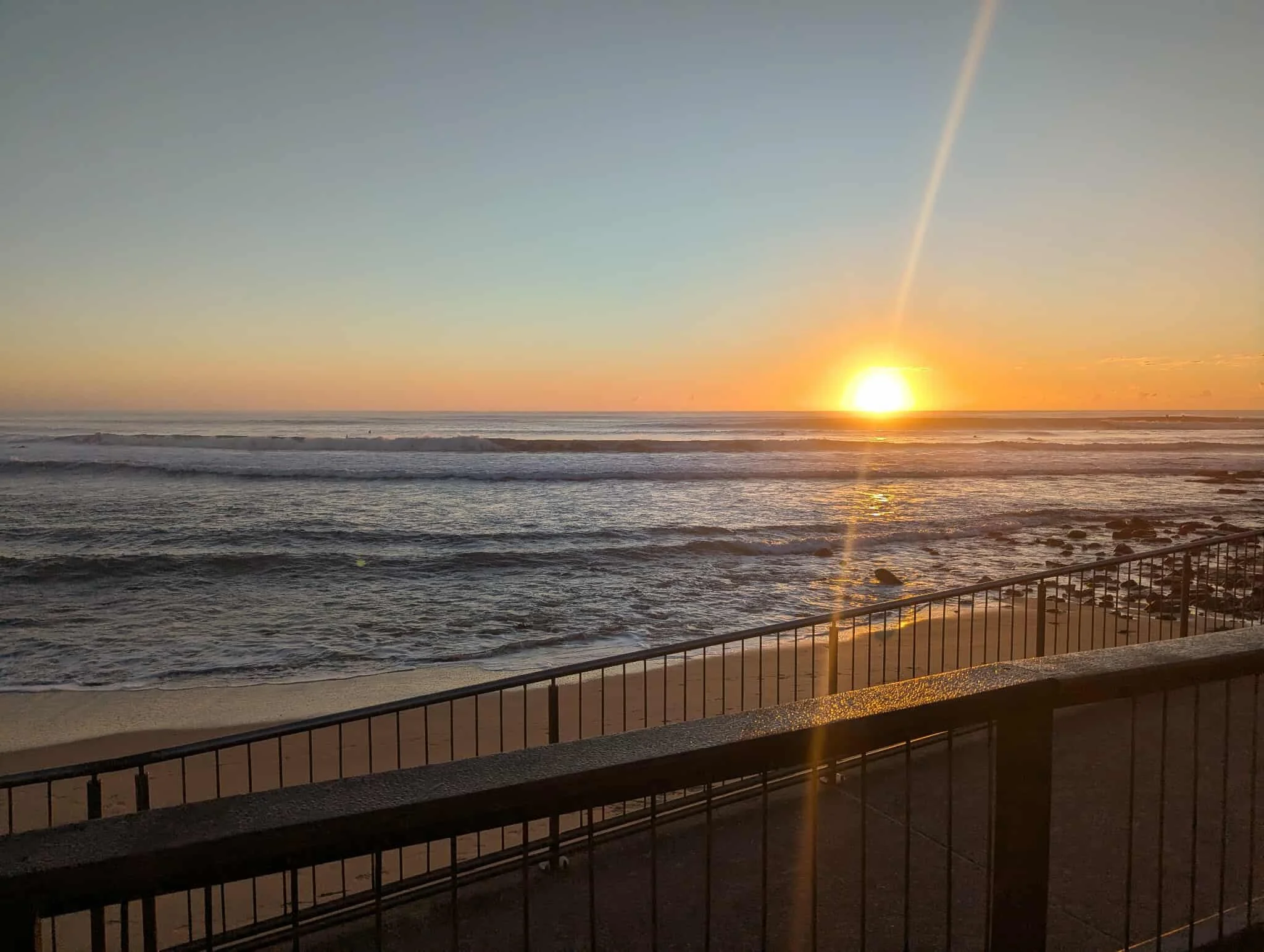 Sunset over the ocean viewed from a balcony with a black metal railing.
