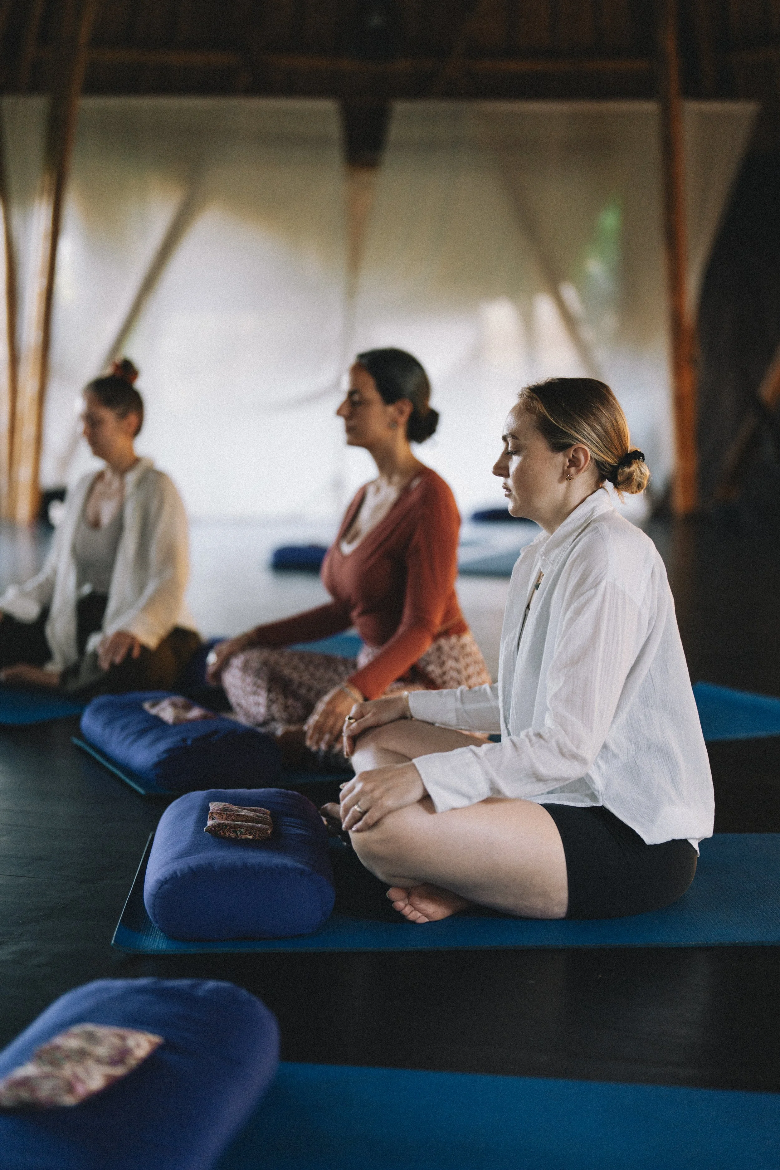 Drei Frauen sitzen im Meditationsraum auf Yoga-Matten, in meditativer Haltung mit geschlossenen Augen, während sie meditieren. AYAMA Events, Frauenkreise in Rapperswil SG 