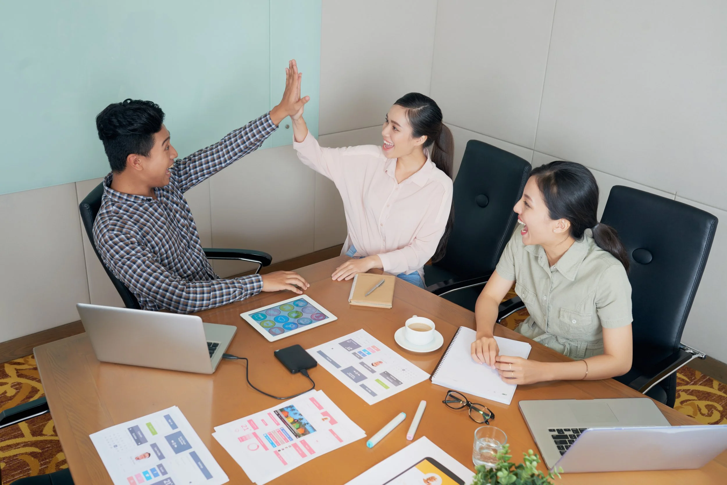 happy-creative-asian-colleagues-sitting-desk-office-doing-high-five.jpg