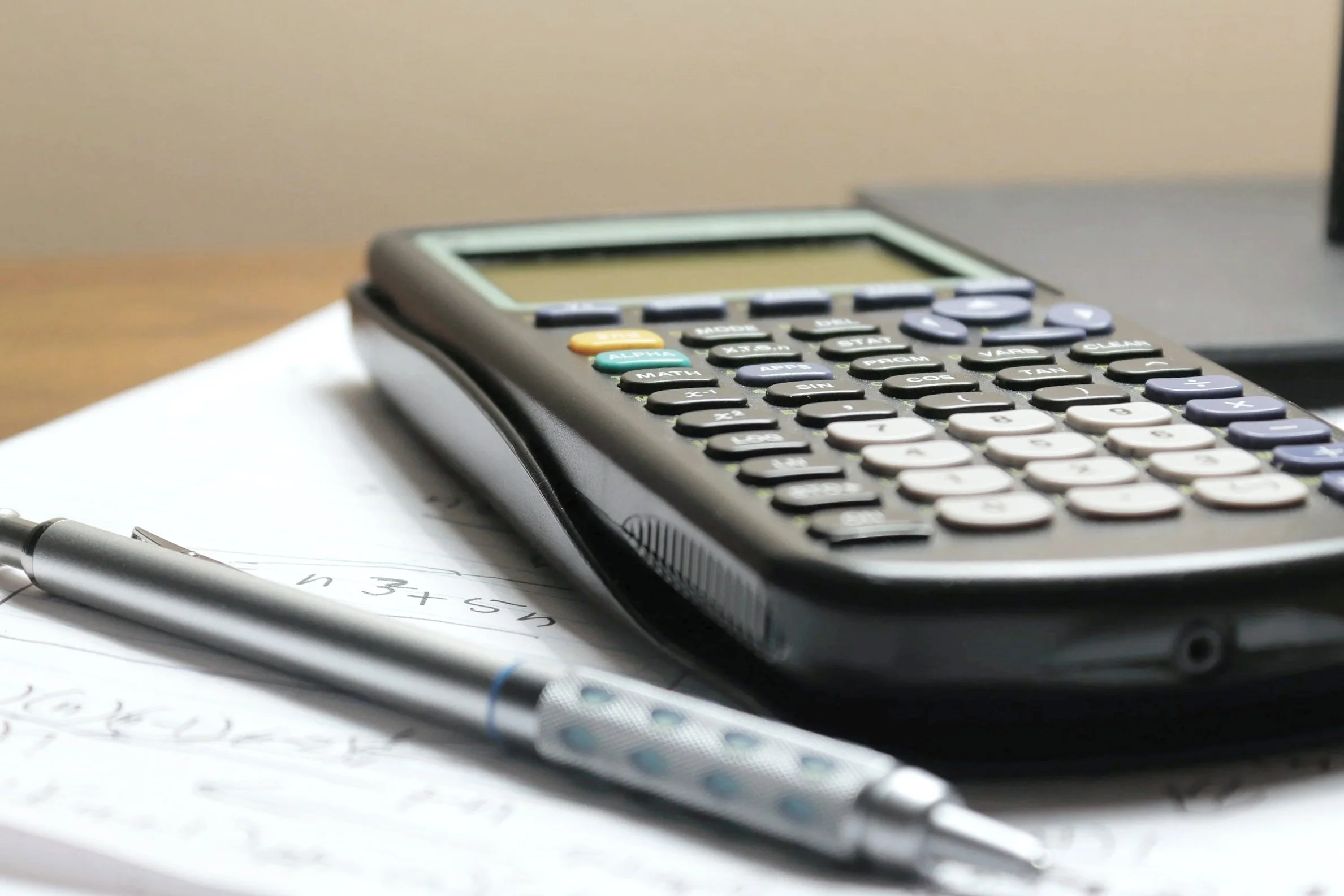 Calculator on a desk with papers and a pen.