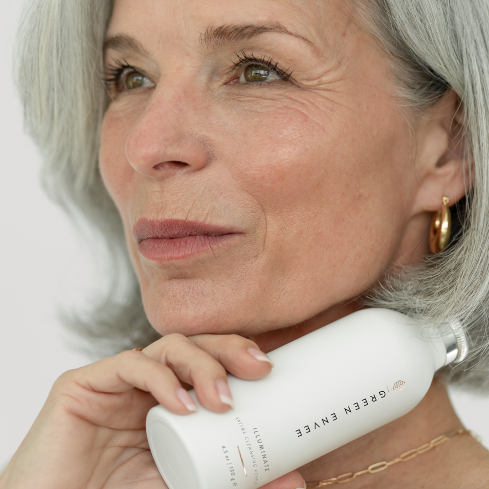Close-up of a mature woman with gray hair holding a skincare product close to her face, with a gentle smile. Toronto natural and holistic skincare line. Toronto botanical skincare line. Toronto organic skincare.