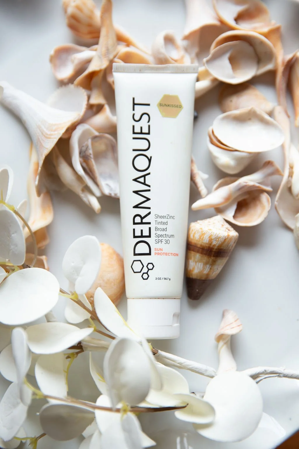 A tube of Supergoop! sunscreen with SPF 30 surrounded by seashells and white flowers on a light background. Toronto cosmeceutical skincare line.