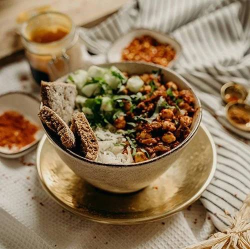 Bol de nourriture avec riz, haricots, légumes, et trois morceaux de pain grillé, accompagné de condiments et d'une tasse de thé ou café.